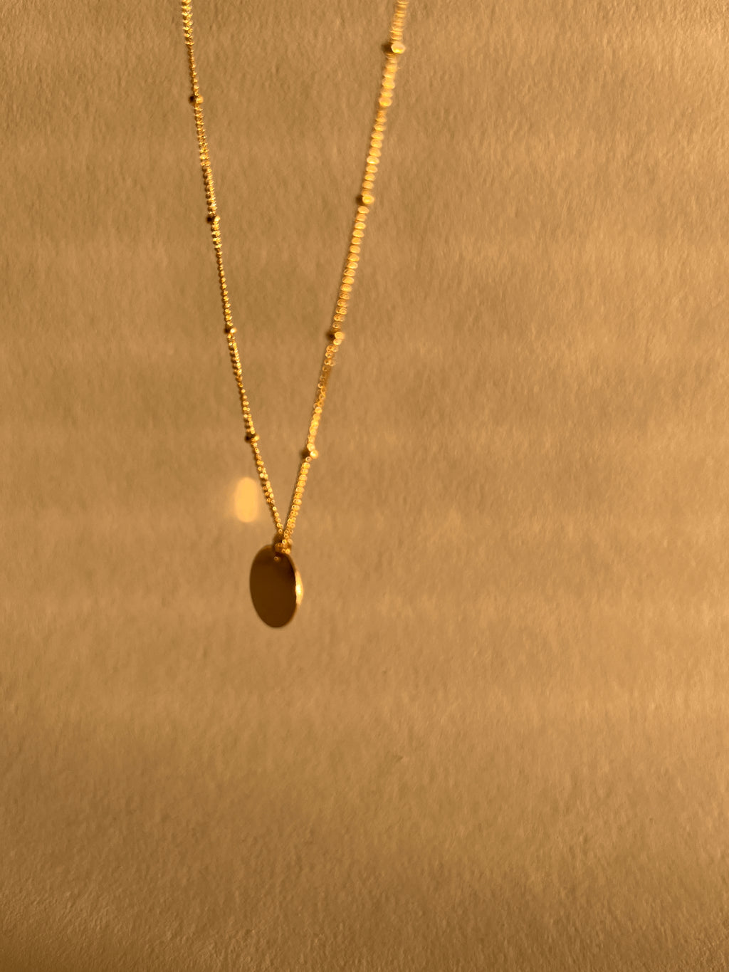 Artistic, slightly blurry shot of the yellow gold-filled My Favorite Necklace swinging in air, emphasizing movement and dainty design