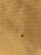 Yellow gold-filled My Favorite Necklace with 1mm fixed beads and a sliding 10mm disc, suspended against a warm neutral sunlit backdrop