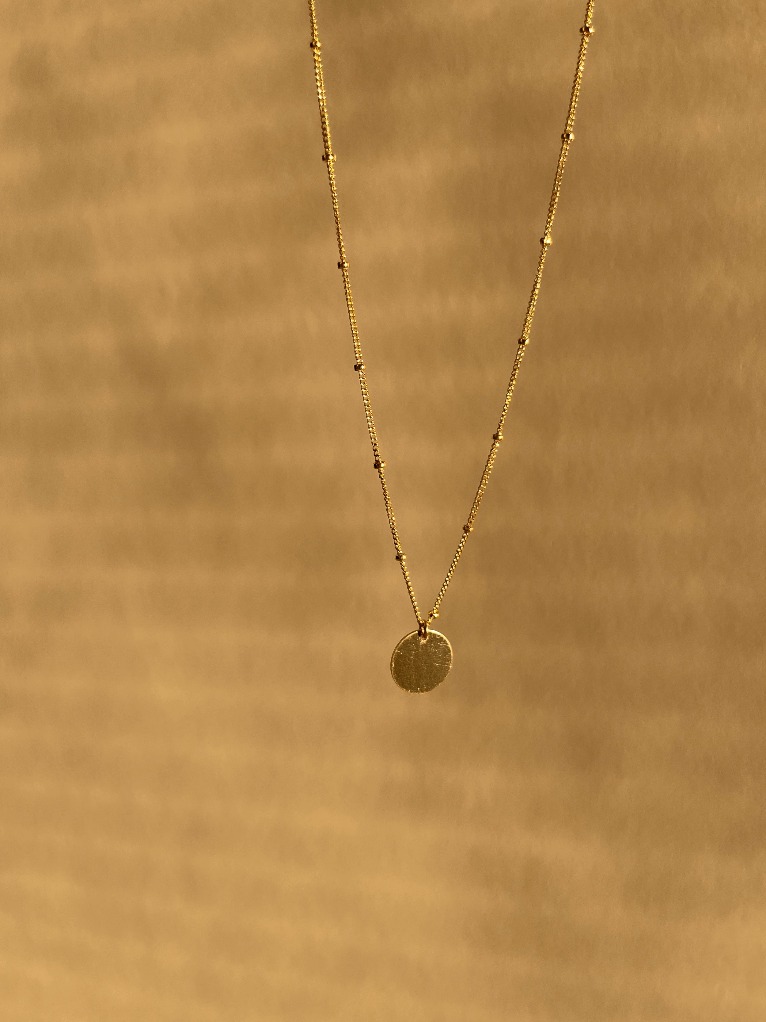 Yellow gold-filled My Favorite Necklace with 1mm fixed beads and a sliding 10mm disc, suspended against a warm neutral sunlit backdrop