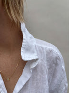 Woman in white collared shirt wearing Thalken dainty minimalist Ethiopian opal necklace in yellow gold-filled.