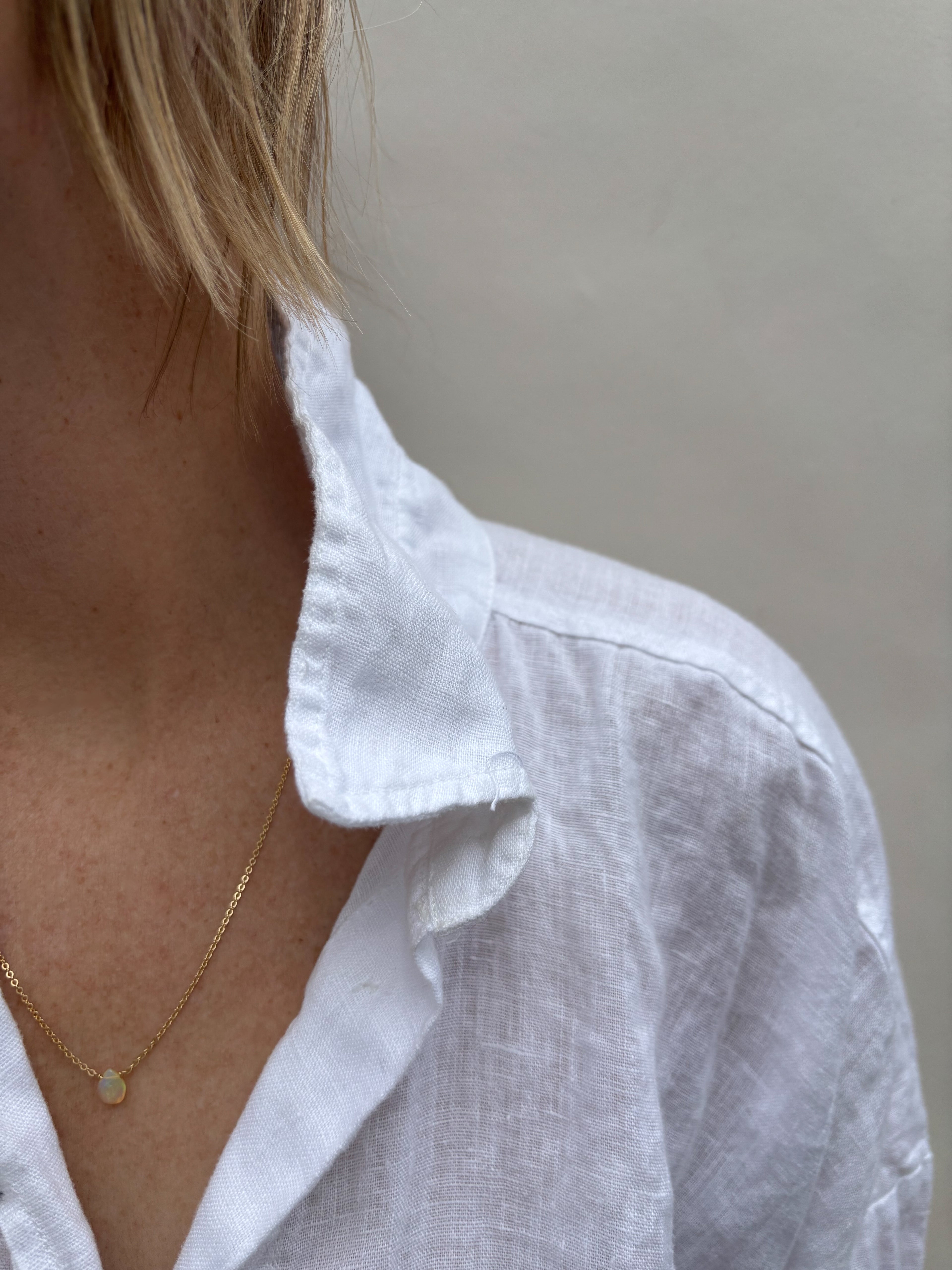 Woman in white collared shirt wearing Thalken dainty minimalist Ethiopian opal necklace in yellow gold-filled.