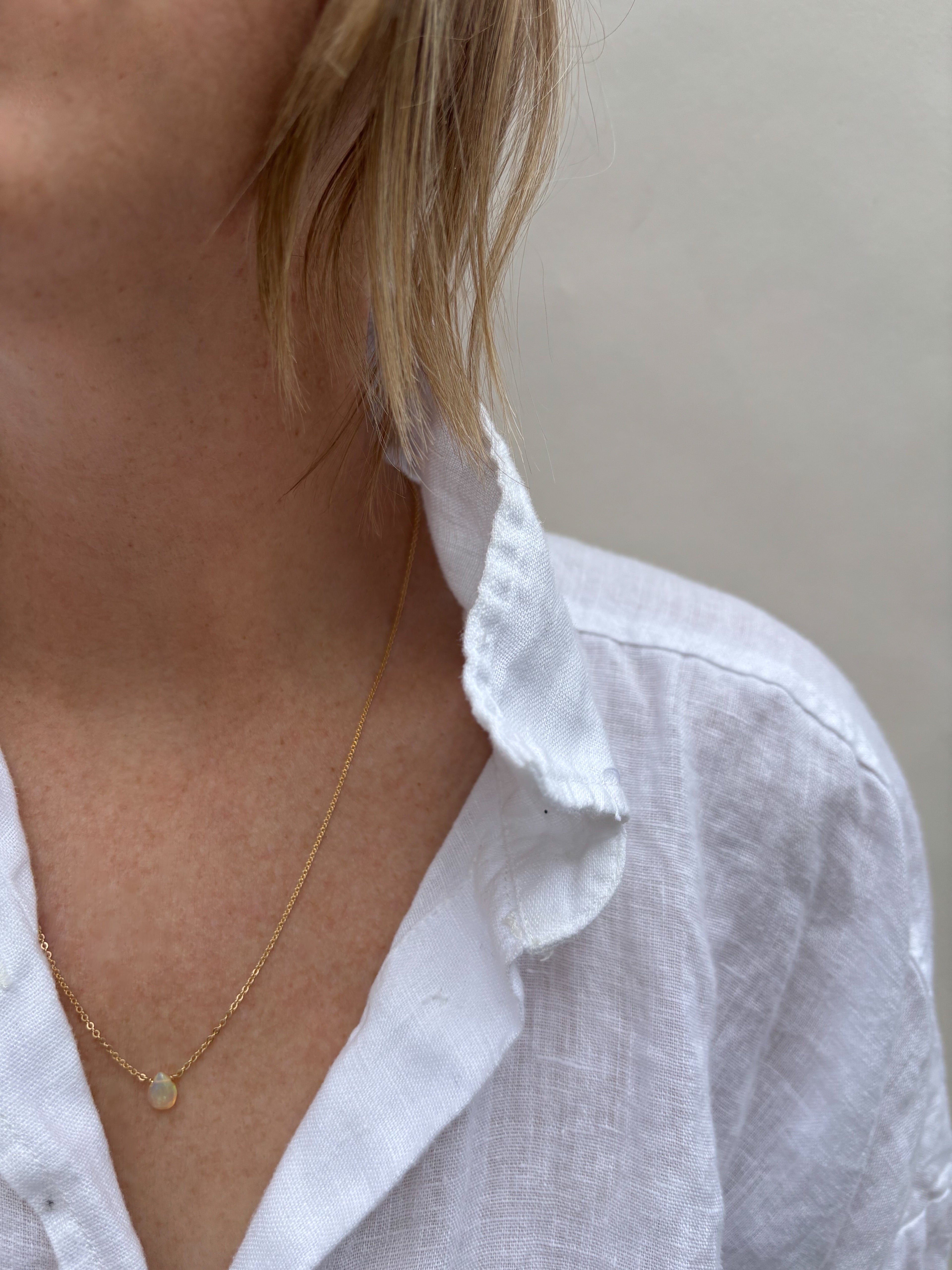 Woman in white linen shirt wearing Thalken dainty minimalist Ethiopian opal necklace in yellow gold-filled 