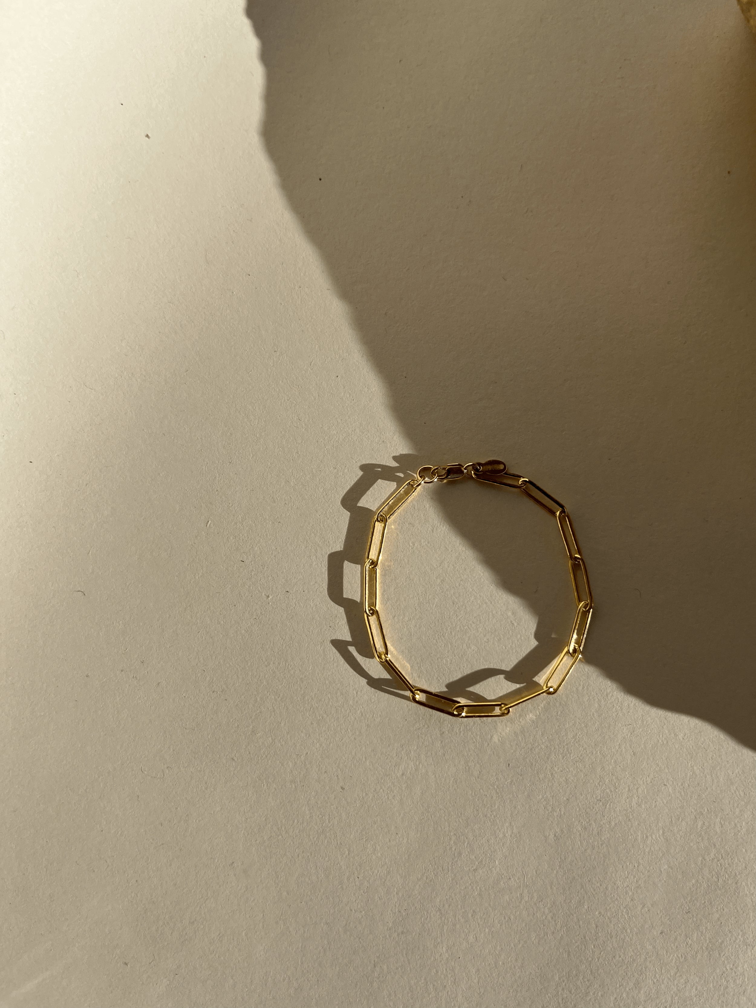 Thalken Large Link Paperclip Bracelet in yellow gold-filled displayed further away on a neutral paper backdrop in warm light