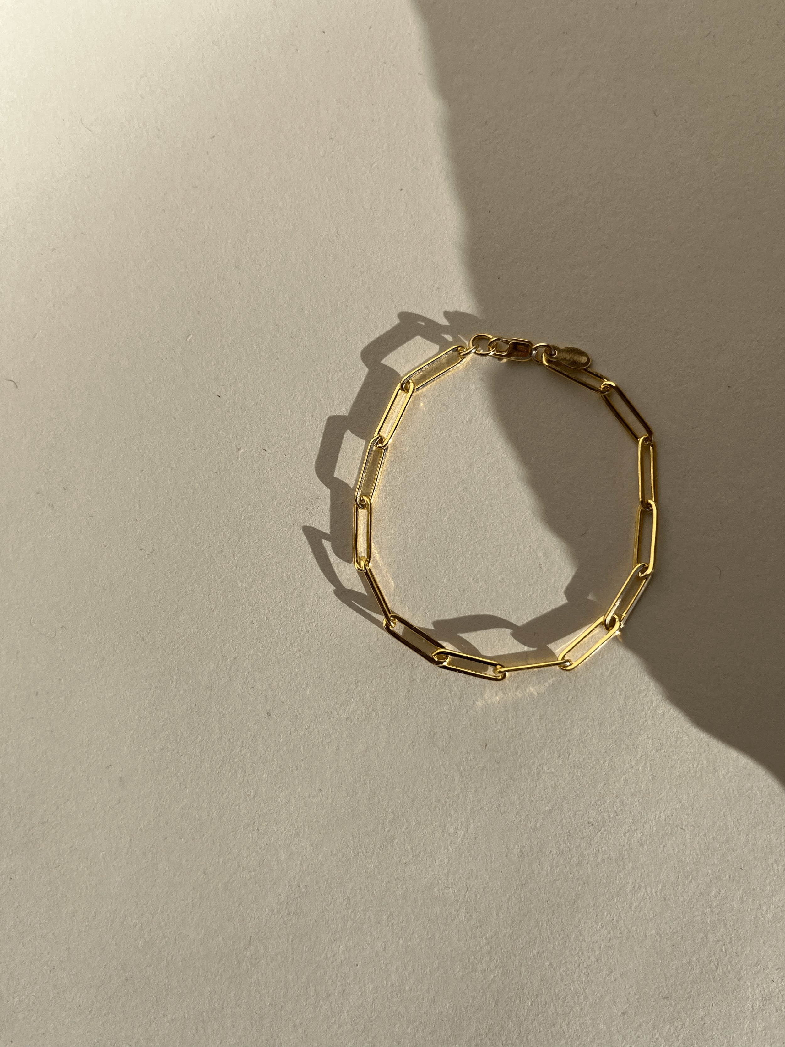 Thalken Large Link Paperclip Bracelet in yellow gold-filled displayed on a neutral paper backdrop in warm light