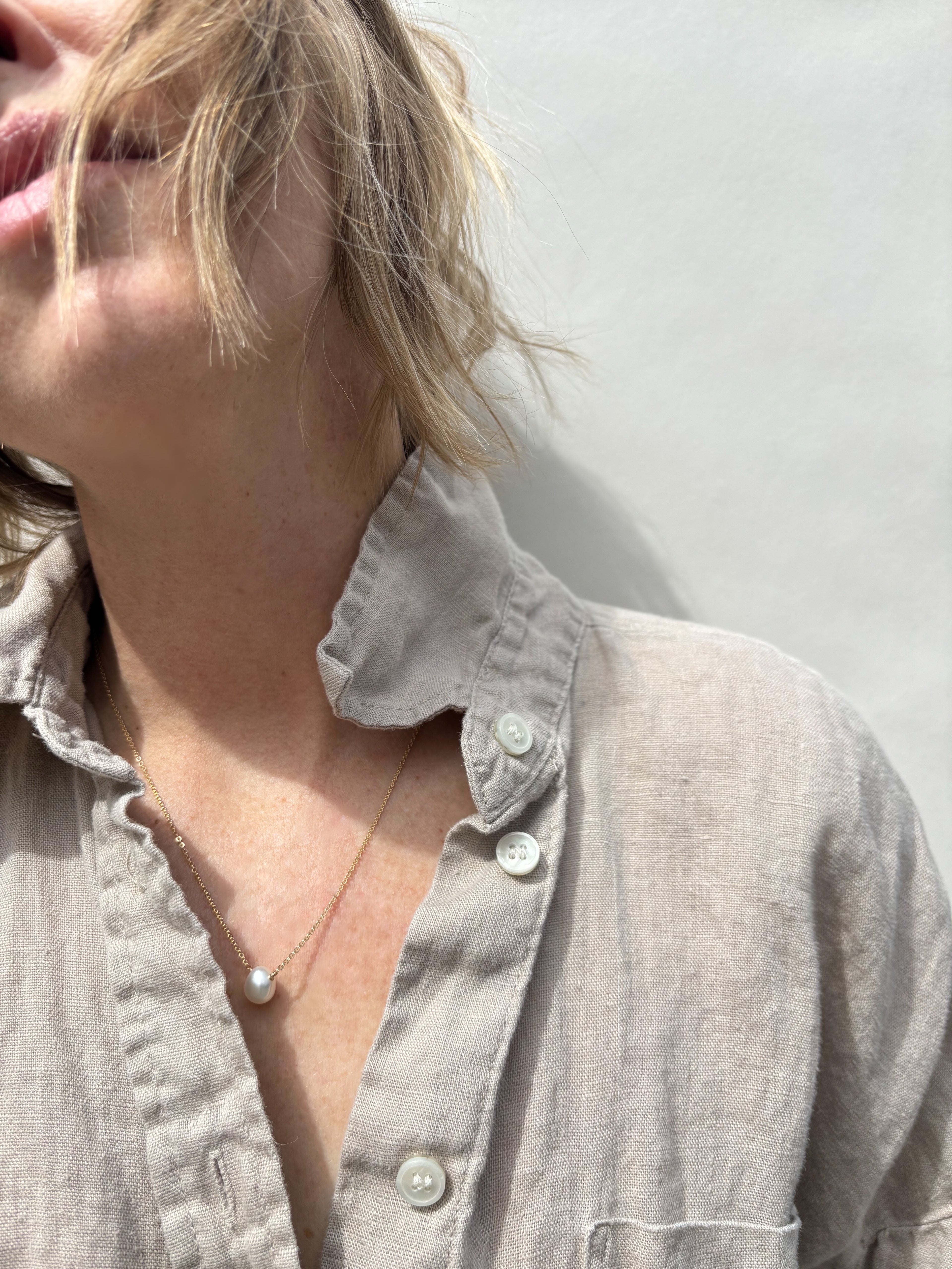 Fixed pearl necklace on woman in tan cotton collared shirt and you can see the bottom of her face