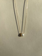 Thalken yellow gold-filled necklace featuring a luminous pearl drop in front of a neutral backdrop