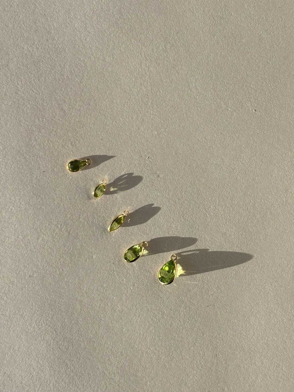 Close-up of individual 14k gold drop charms in various shapes and sizes, ready to be attached to Thalken hoop earrings