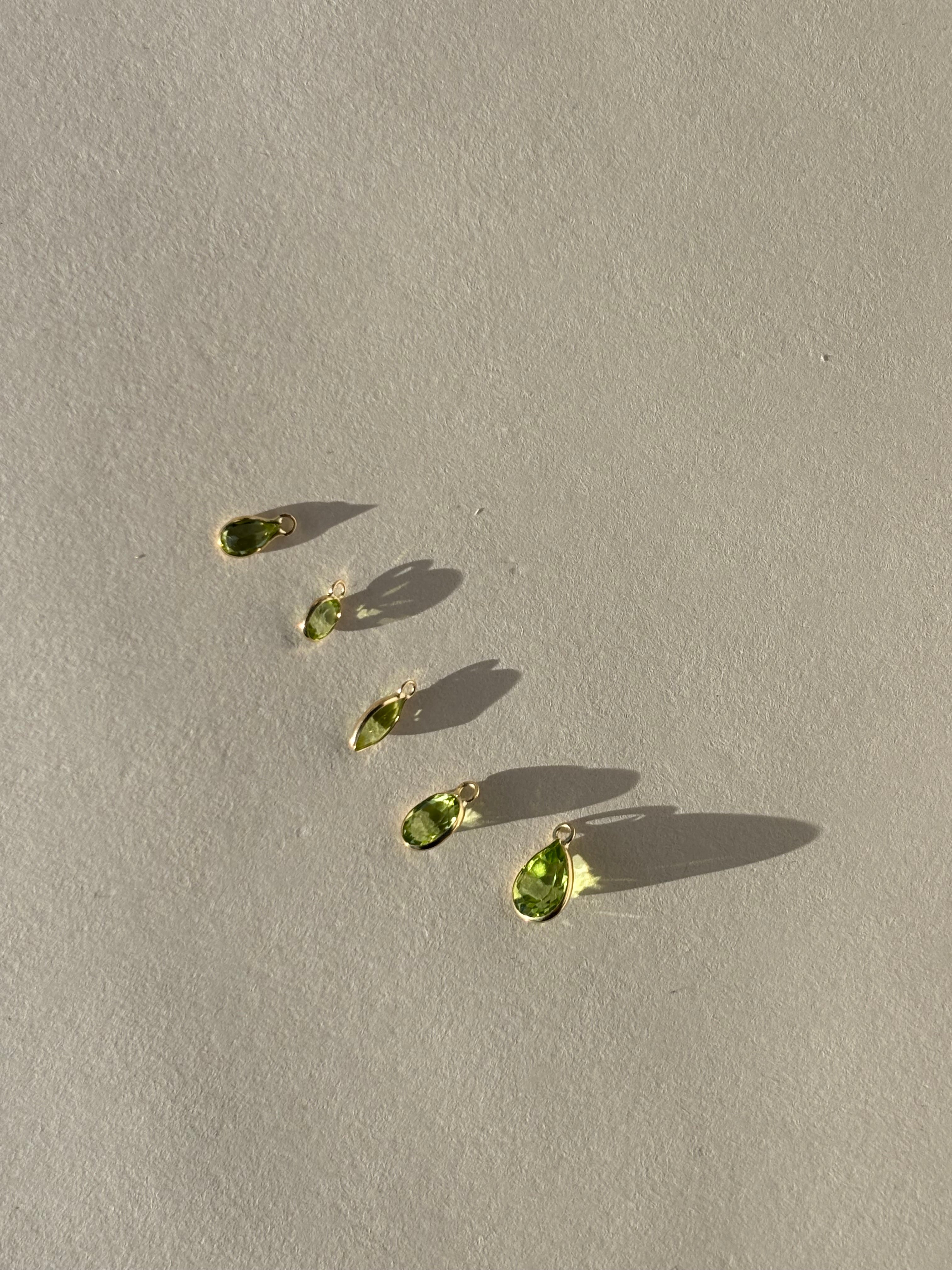 Close-up of individual 14k gold drop charms in various shapes and sizes, ready to be attached to Thalken hoop earrings