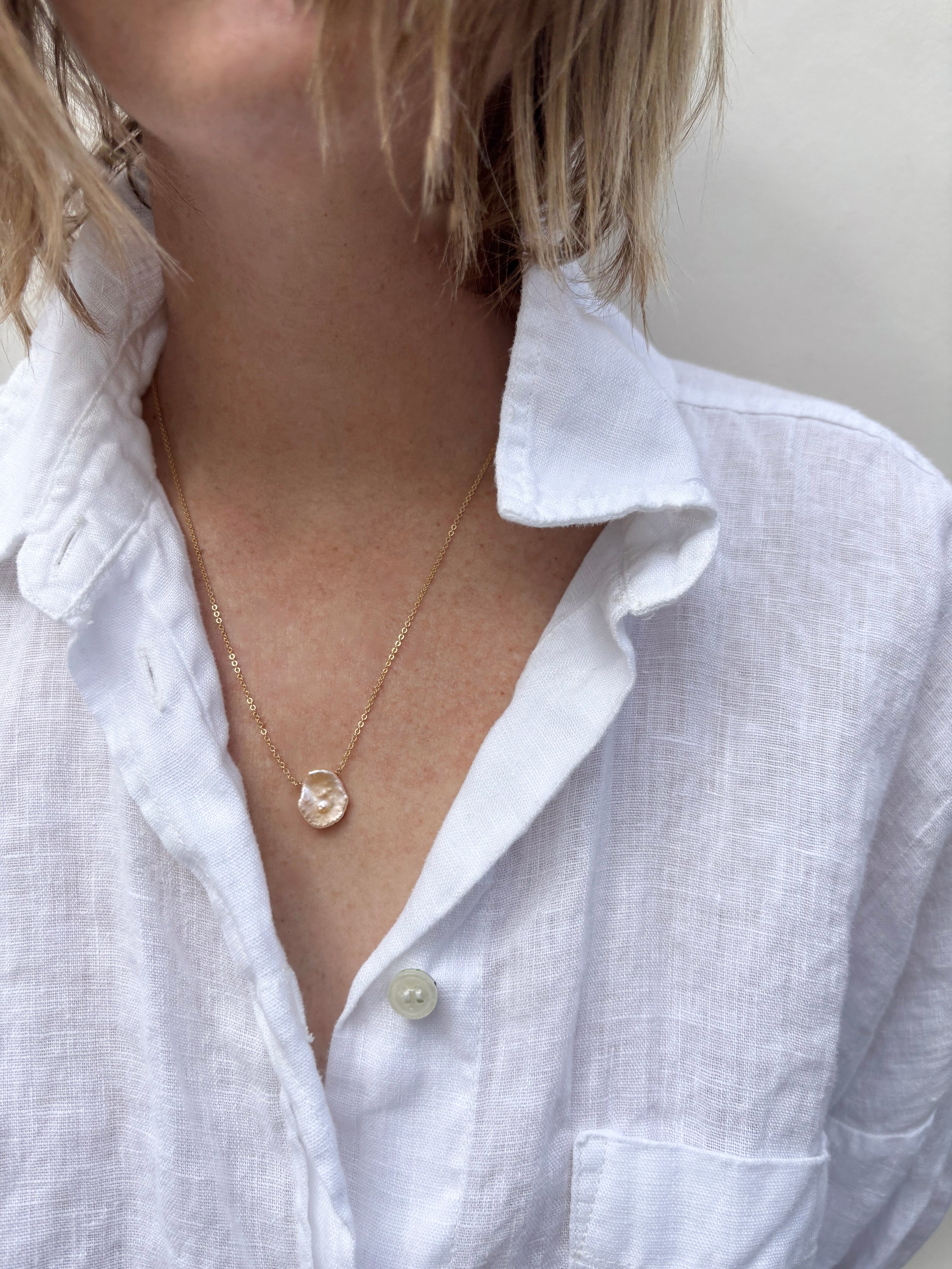 Woman wearing a flat freshwater pink pearl resembling a petal fixed on a dainty yellow gold-filled chain