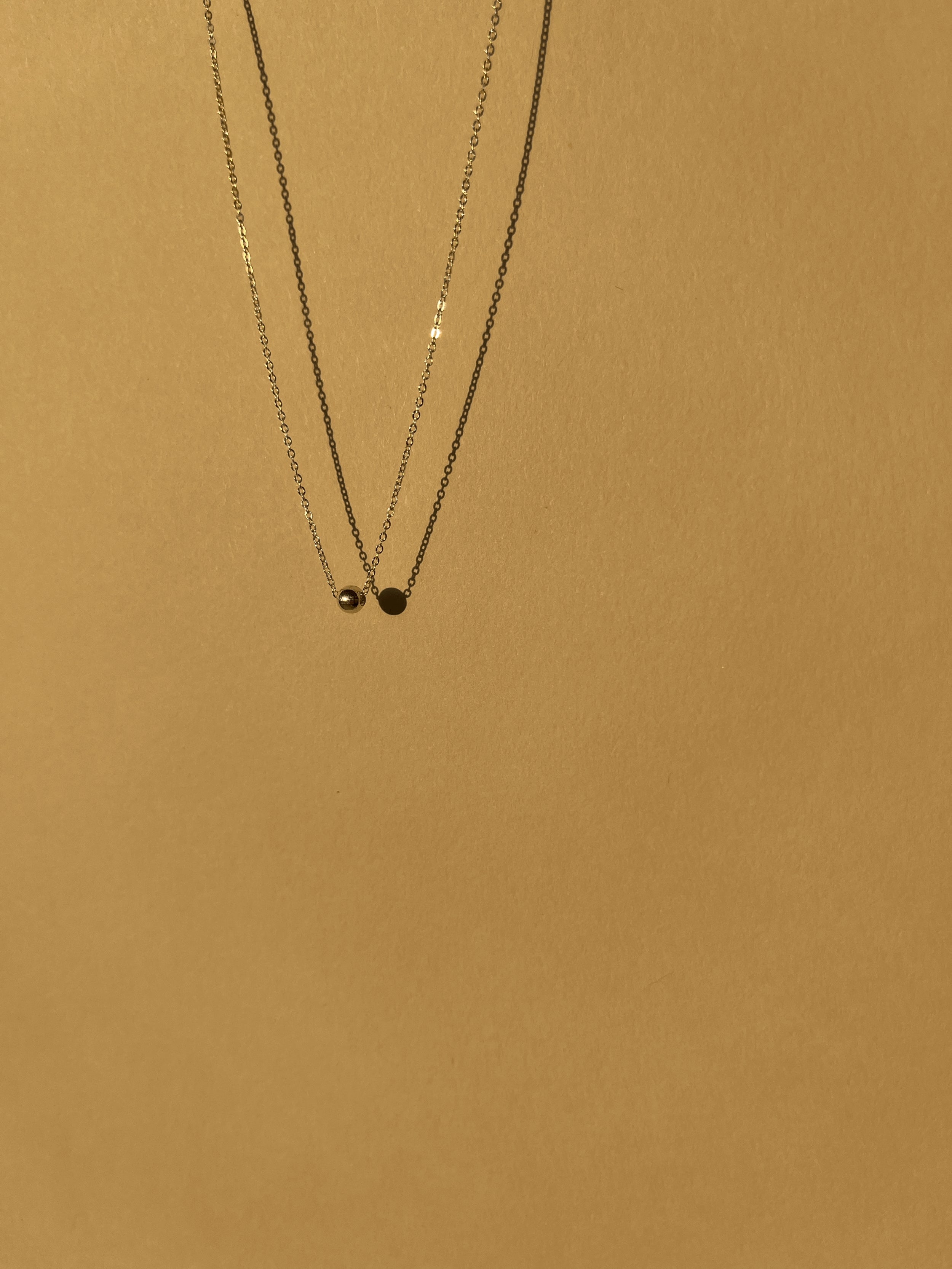 Sterling silver Petite Ball Choker necklace floating against a sunlit neutral backdrop, emphasizing its delicate 4mm accent bead and dainty chain