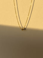 Close-up of the yellow gold-filled Petite Ball Choker highlighting the delicate chain and 4mm sliding accent bead, warm neutral sunlit background