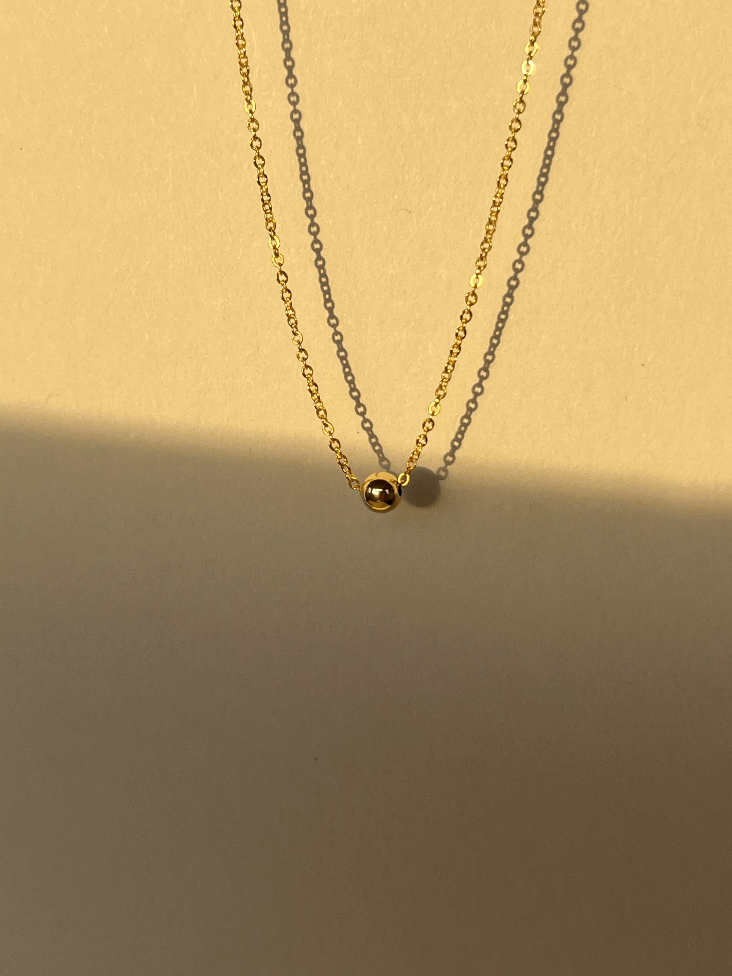Close-up of the yellow gold-filled Petite Ball Choker highlighting the delicate chain and 4mm sliding accent bead, warm neutral sunlit background
