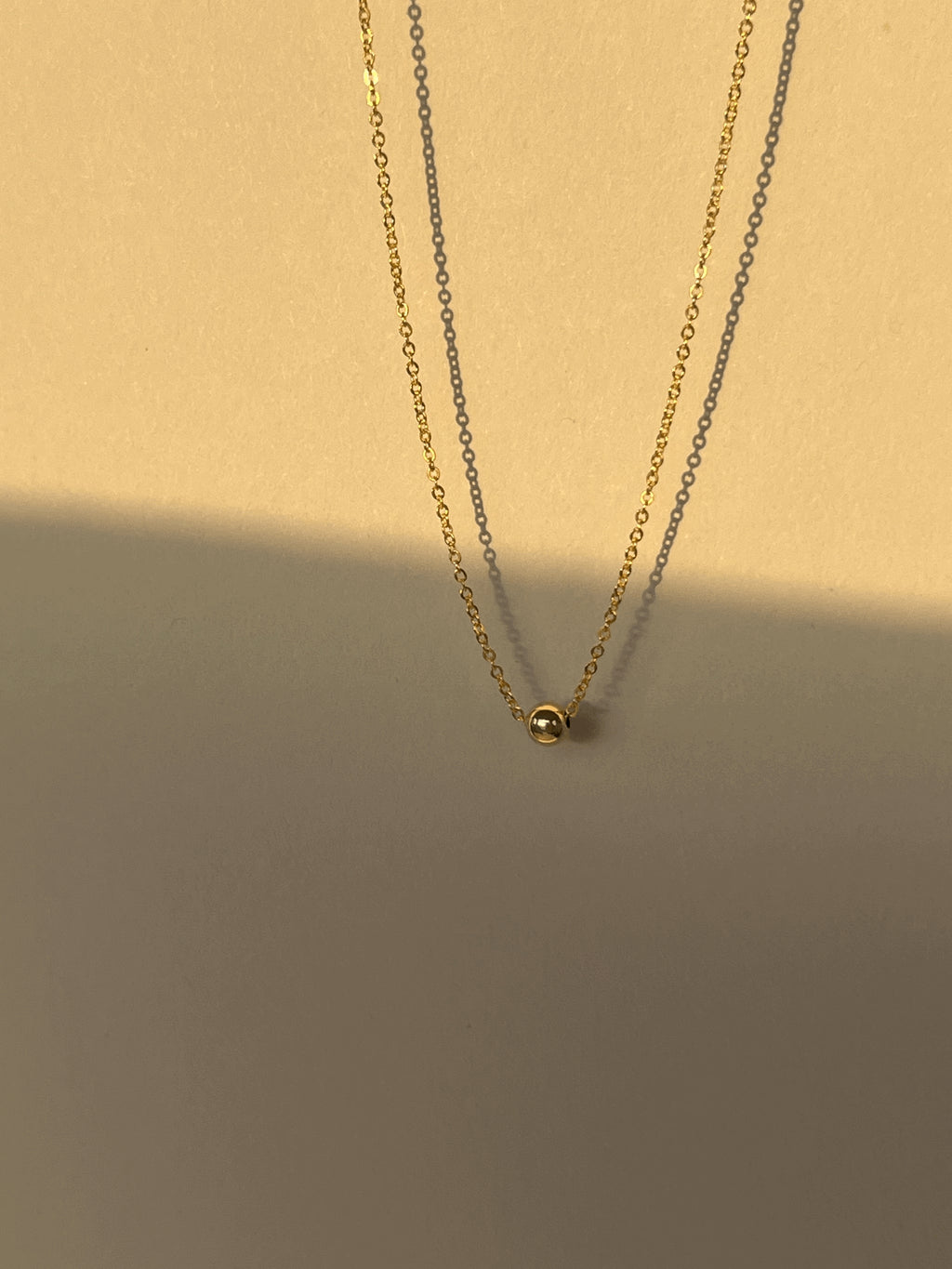 Shot of the yellow gold-filled Petite Ball Choker floating against a warm, softly glowing neutral backdrop, showcasing its dainty design