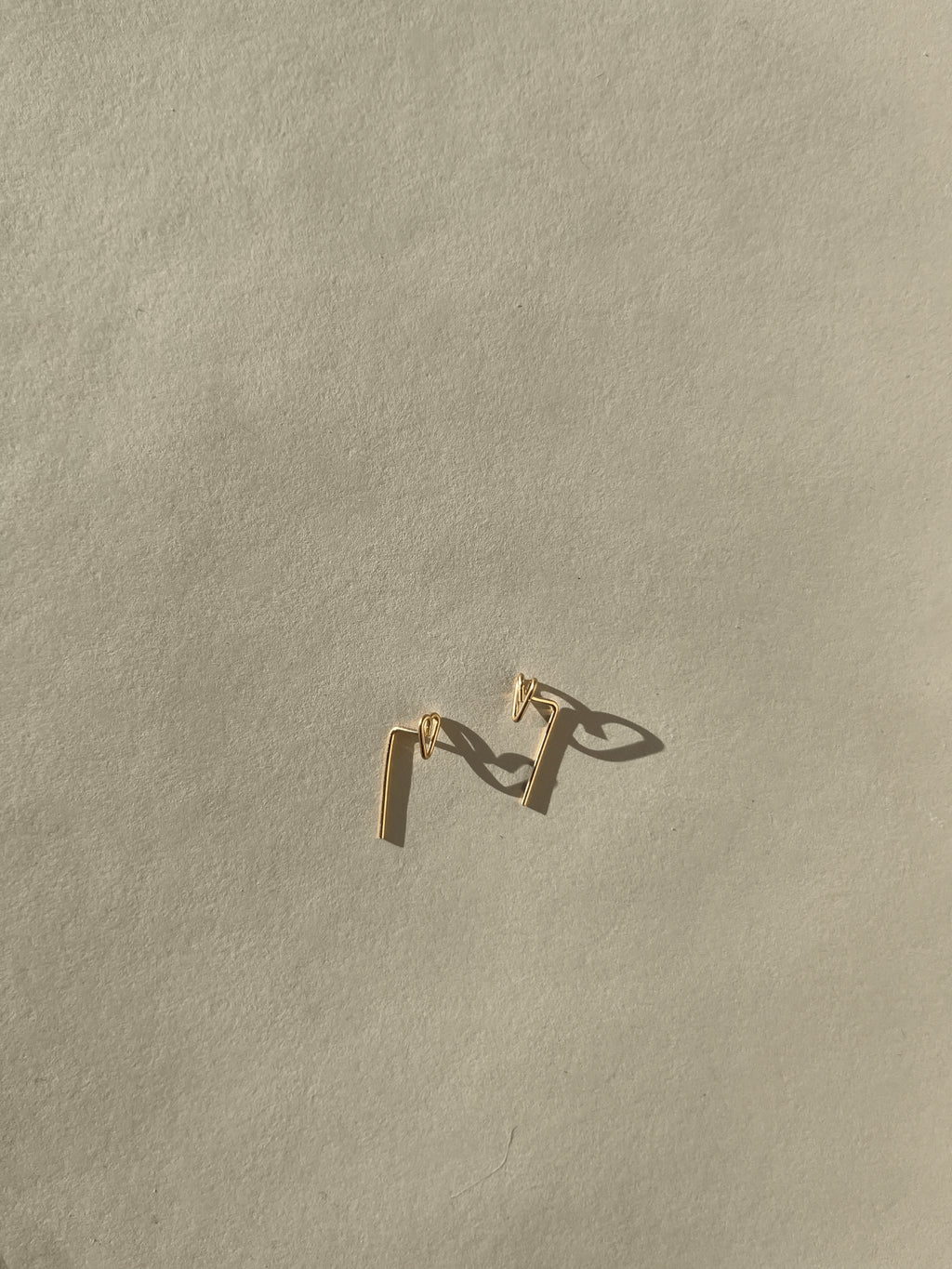 Petite Heart Drop-Back Earrings with a handmade heart front and bent post dropping behind the ear, in gold-filled, on a neutral backdrop by Thalken