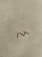 Petite Heart Drop-Back Earrings with a handmade heart front and bent post dropping behind the ear, in gold-filled, on a neutral backdrop by Thalken