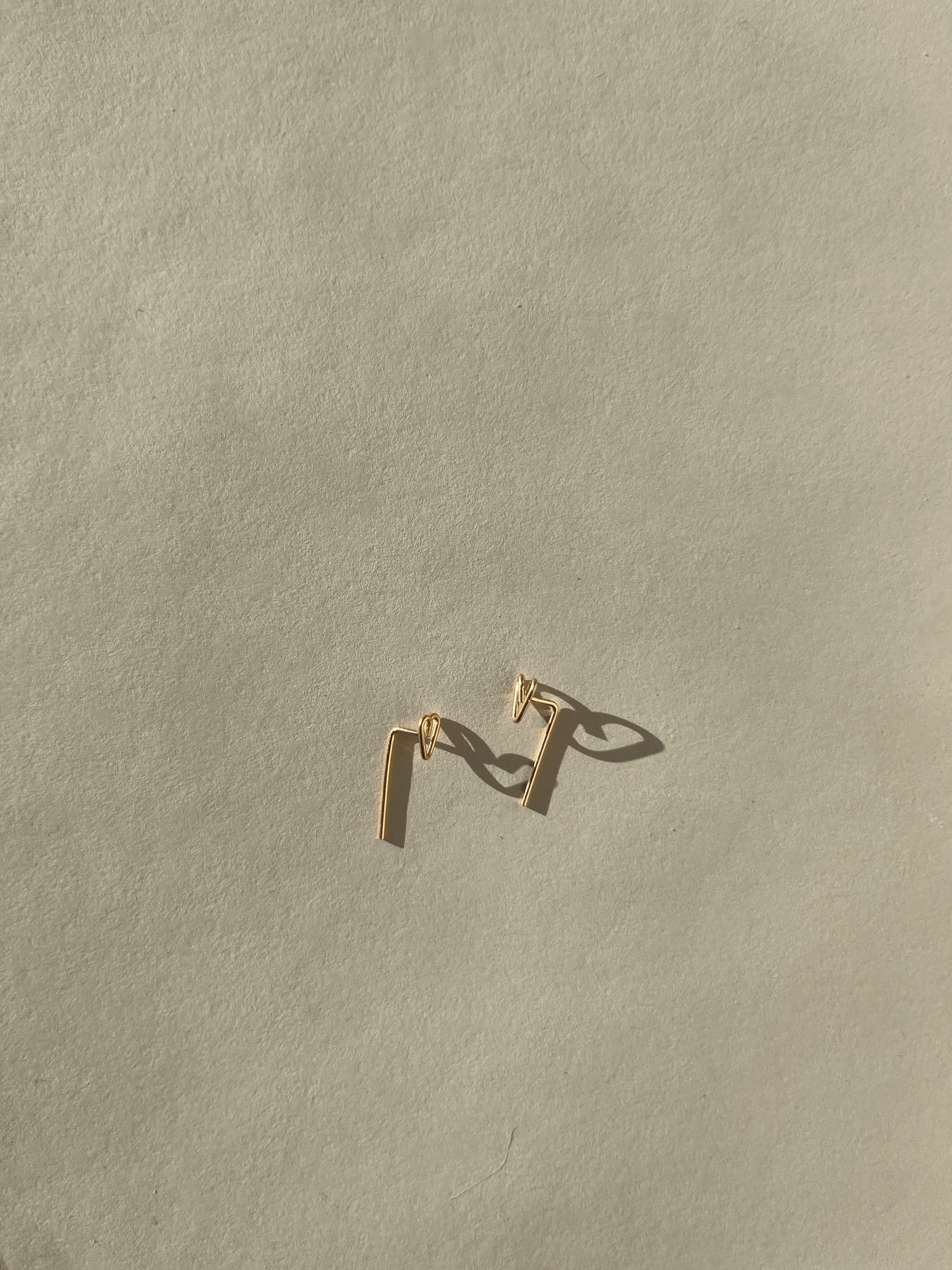 Petite Heart Drop-Back Earrings with a handmade heart front and bent post dropping behind the ear, in gold-filled, on a neutral backdrop by Thalken