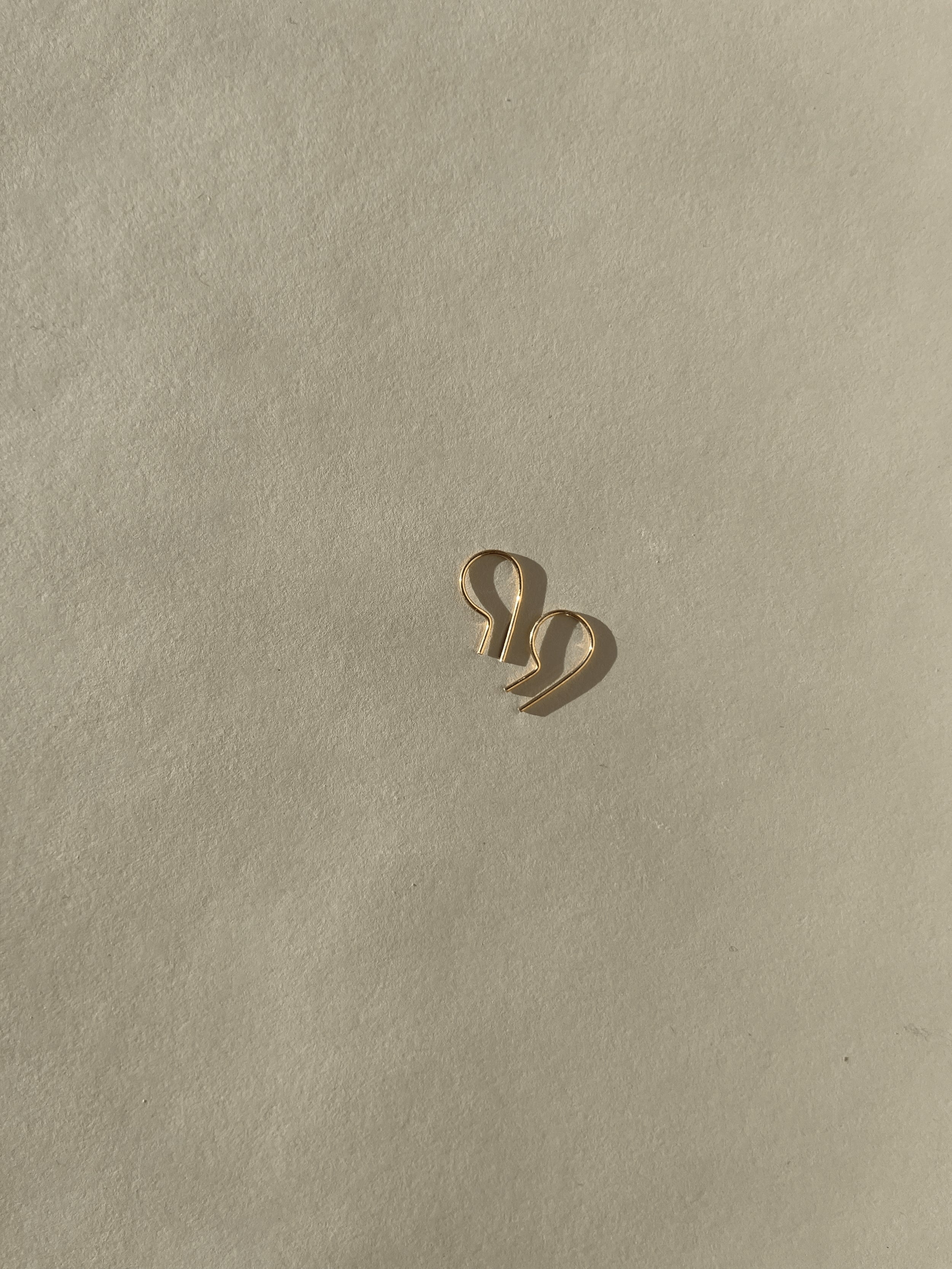 Distant shot of a pair of Petite R Staple Earrings in yellow gold-filled, showcasing its sleek, modern R-shaped design with a polished finish