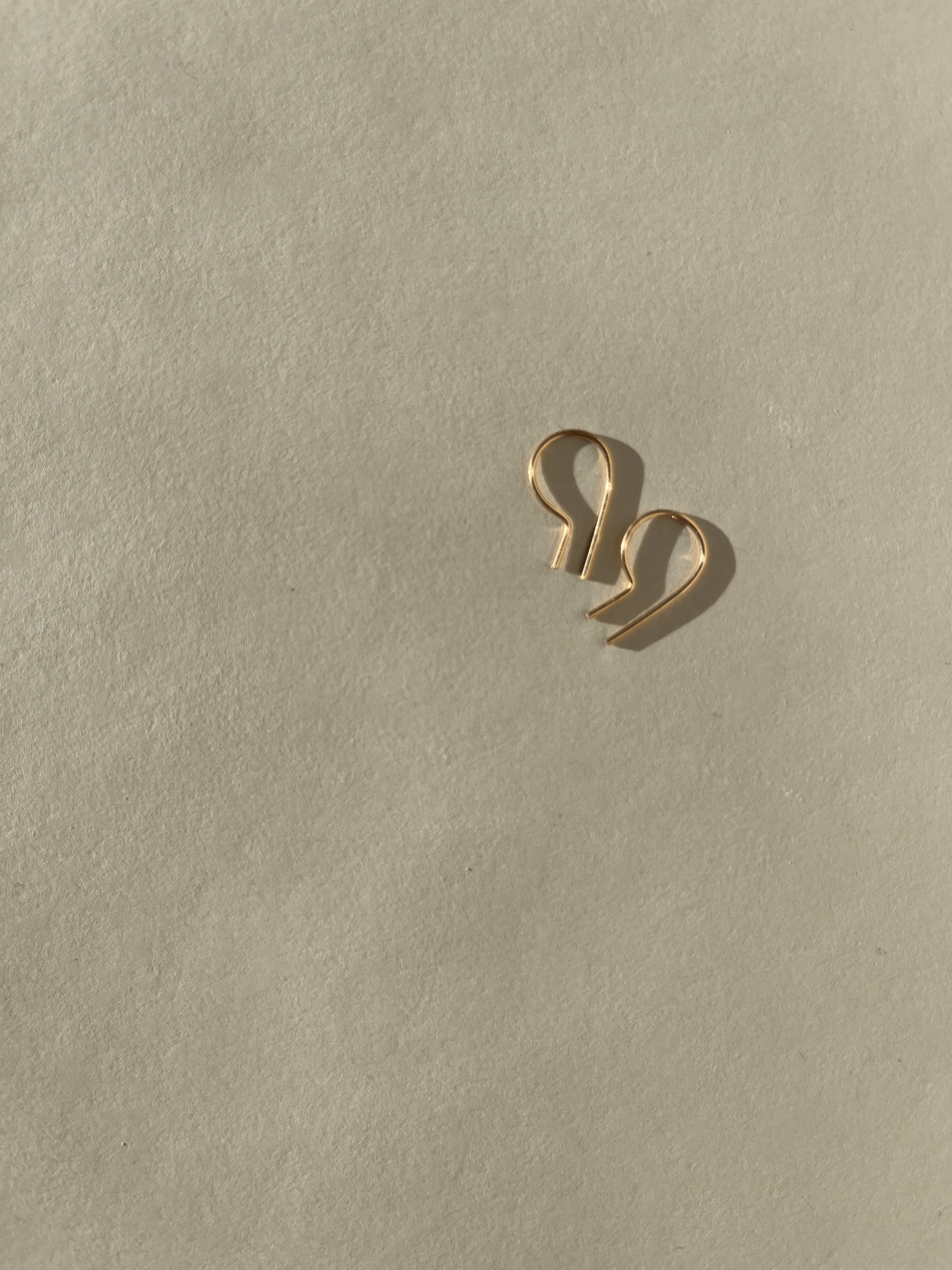 Close-up of a pair of Petite R Staple Earrings in yellow gold-filled, showcasing its sleek, modern R-shaped design with a polished finish