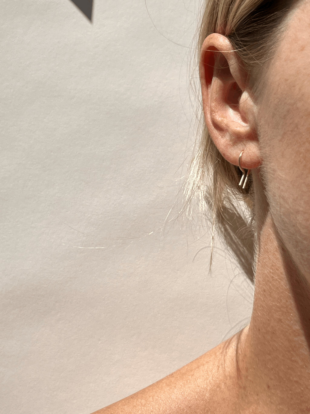 Sunny shot of Petite R Staple Earring in yellow gold-filled in models first ear piercing