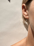 Sunny shot of Petite R Staple Earring in yellow gold-filled in models first ear piercing