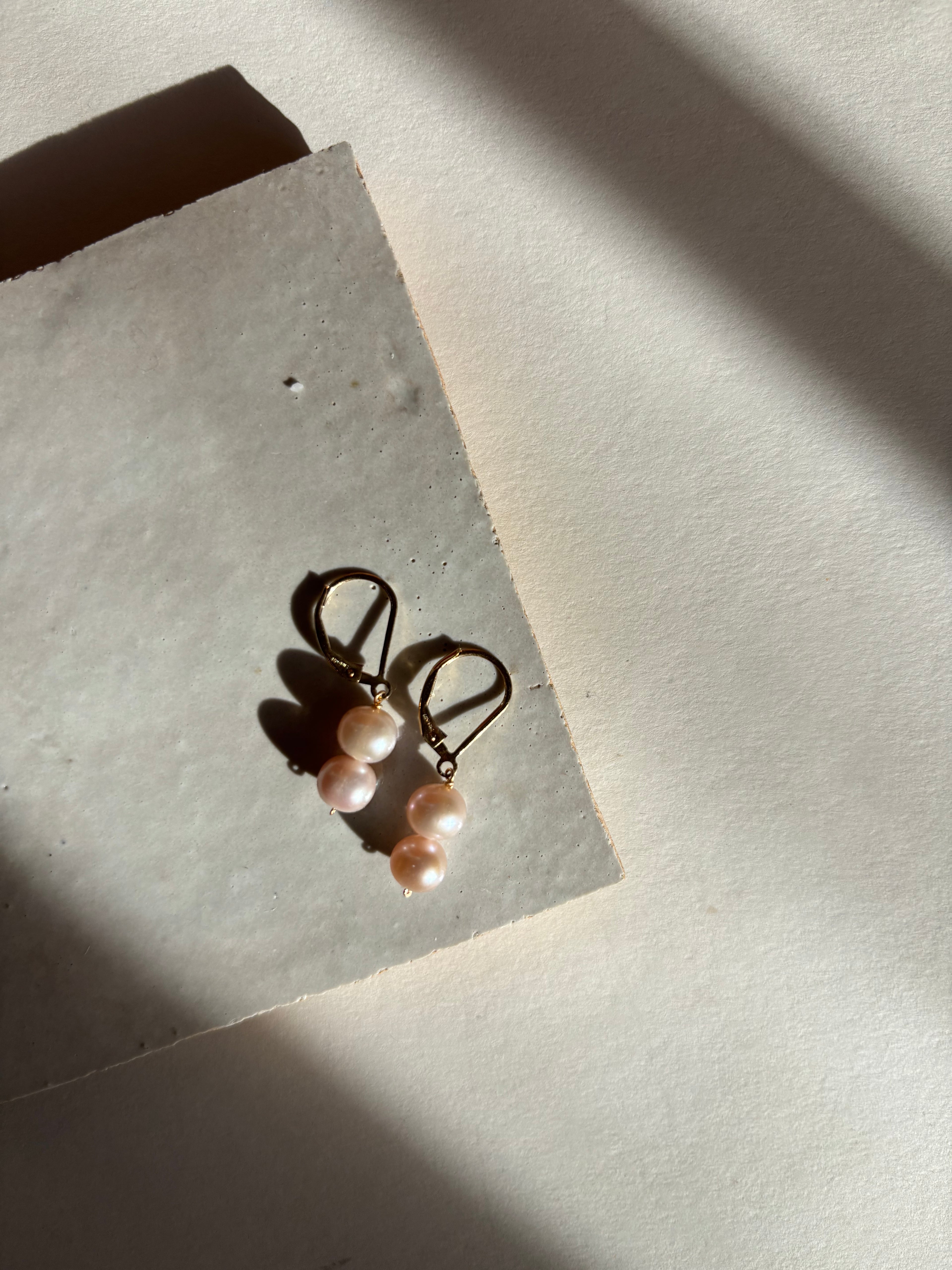 Close-up of the blush (soft pink) double pearl drop detail on leverback earrings with warm, moody lighting.