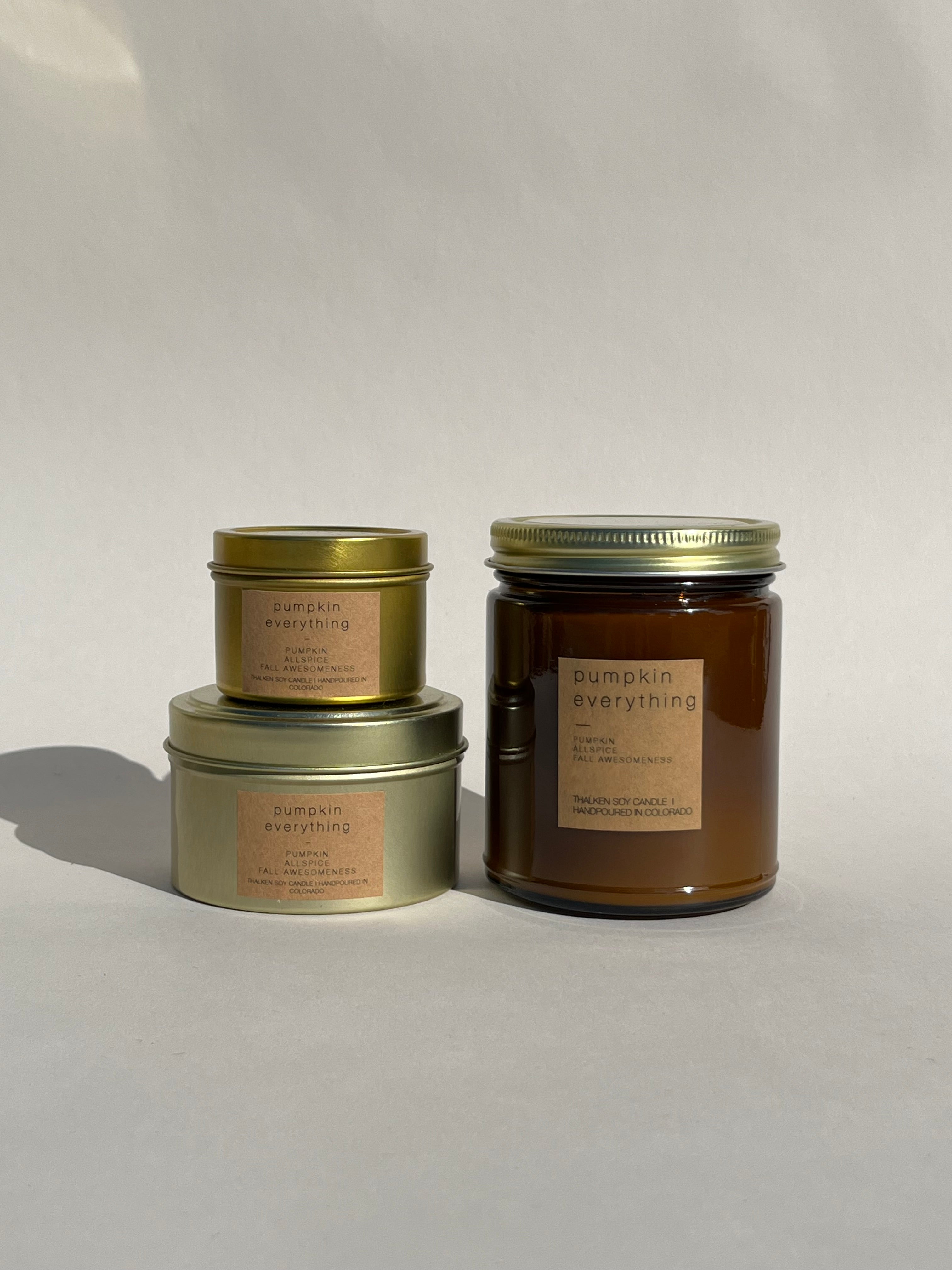 Three Thalken Pumpkin Everything candles: small gold tin, medium gold tin, and large brown glass jar