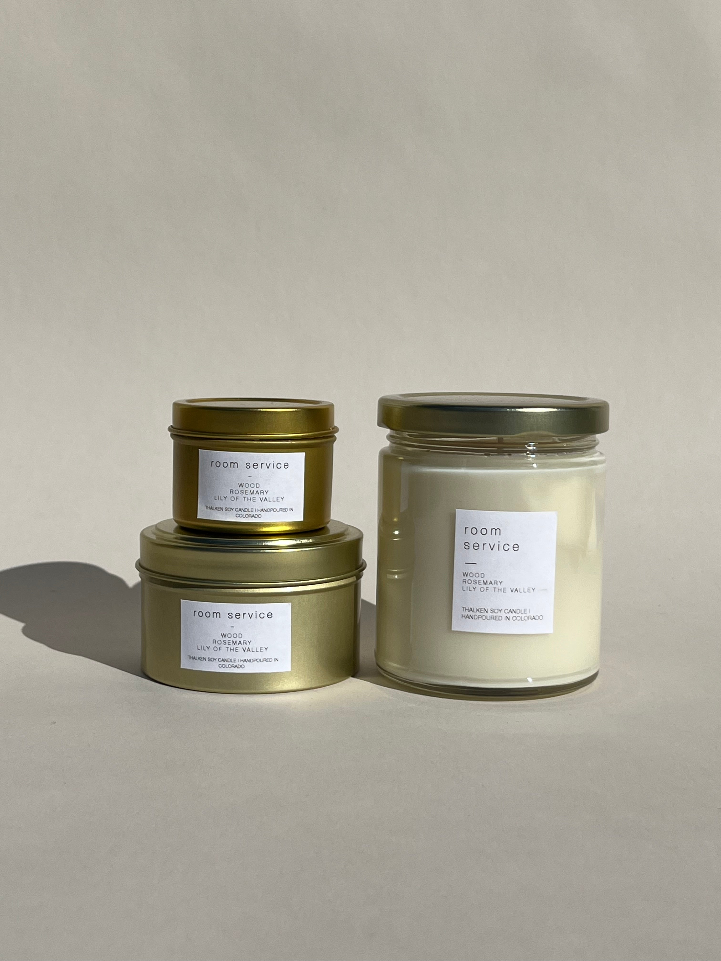 Thalken® Room Service candles in three sizes — 2oz and 6oz gold tins and 8oz soft-glow glass jar. Scent profile: fresh, aromatic, and clean with notes of wood, rosemary, and lily of the valley