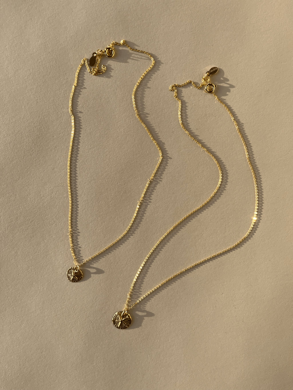 Full product shot of both Sand Dollar Necklaces, 10mm and 12mm charms, displayed on a neutral background