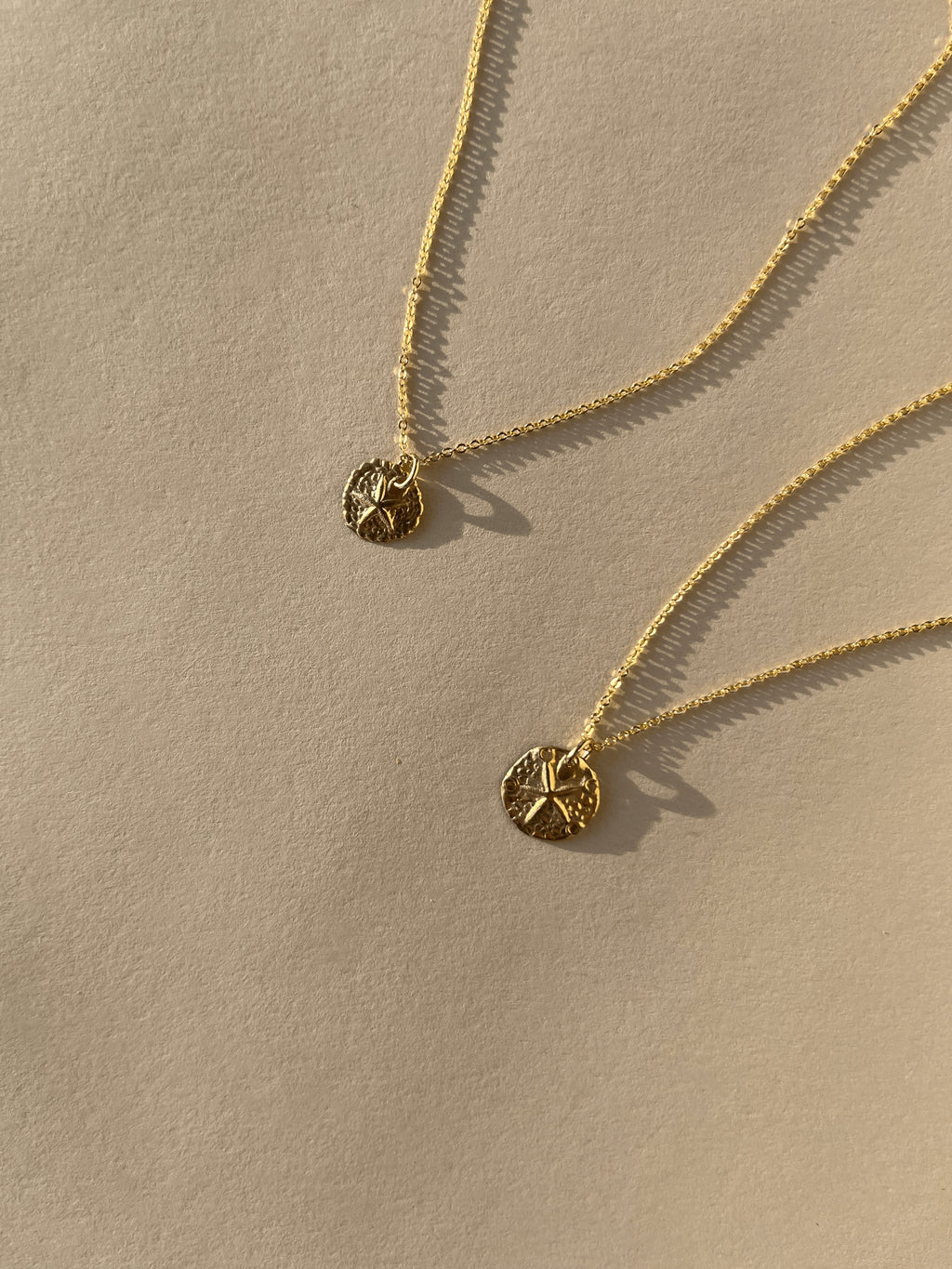 Partial close-up of both Sand Dollar Necklaces, highlighting charm details and chain texture