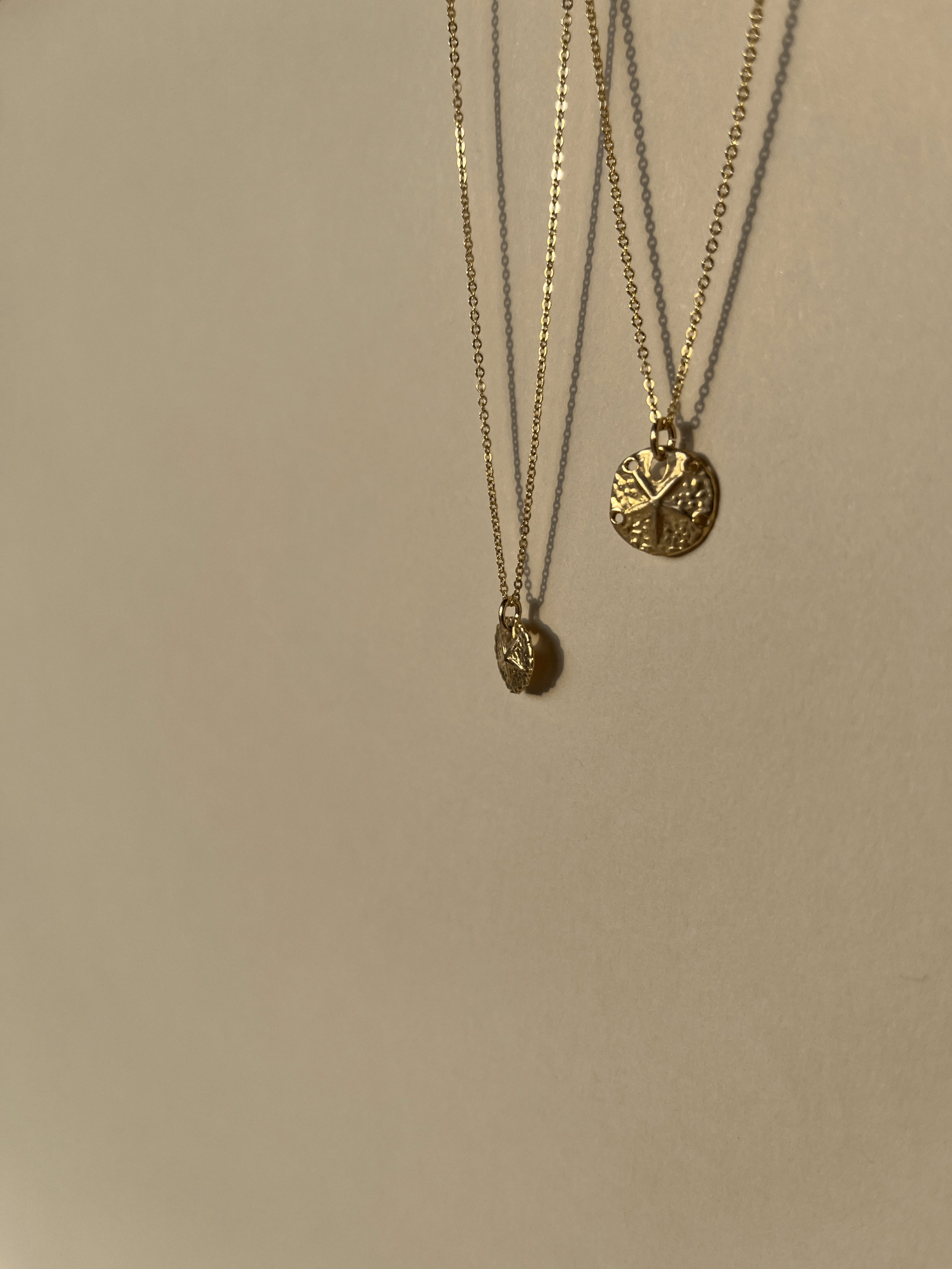 Partial shot of both Sand Dollar Necklaces suspended in the air, emphasizing lightweight, minimalist design
