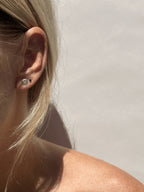 Model wearing small sterling silver sand dollar stud in first ear piercing and tiny black CZ stud in second