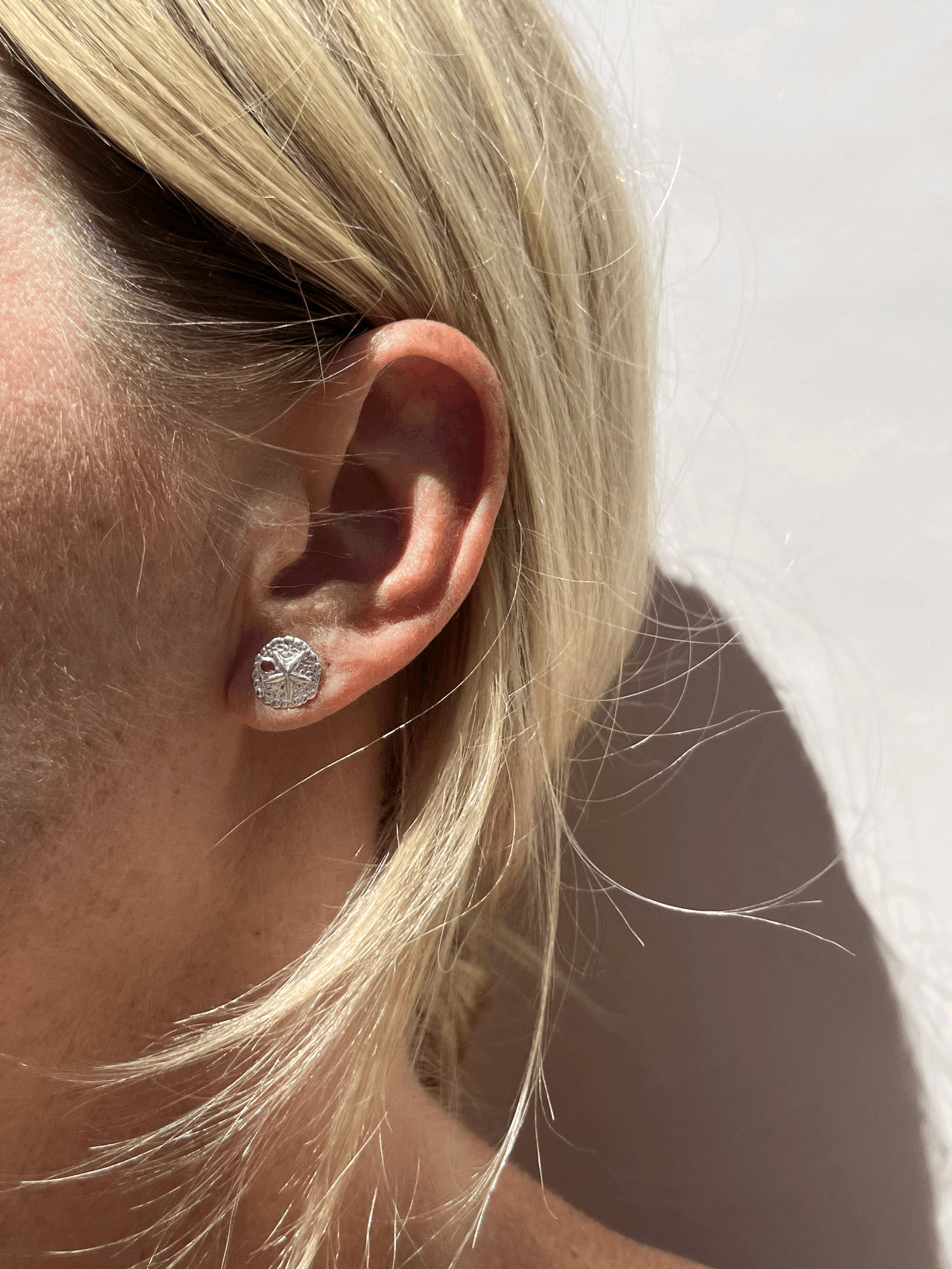 Model wearing large sterling silver sand dollar studs in first ear piercings