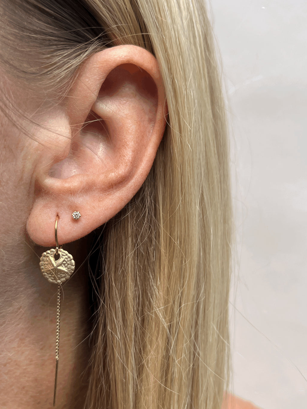 Close-up view of the 10mm yellow gold-filled sand dollar threader earring paired with a small clear crystal stud earring