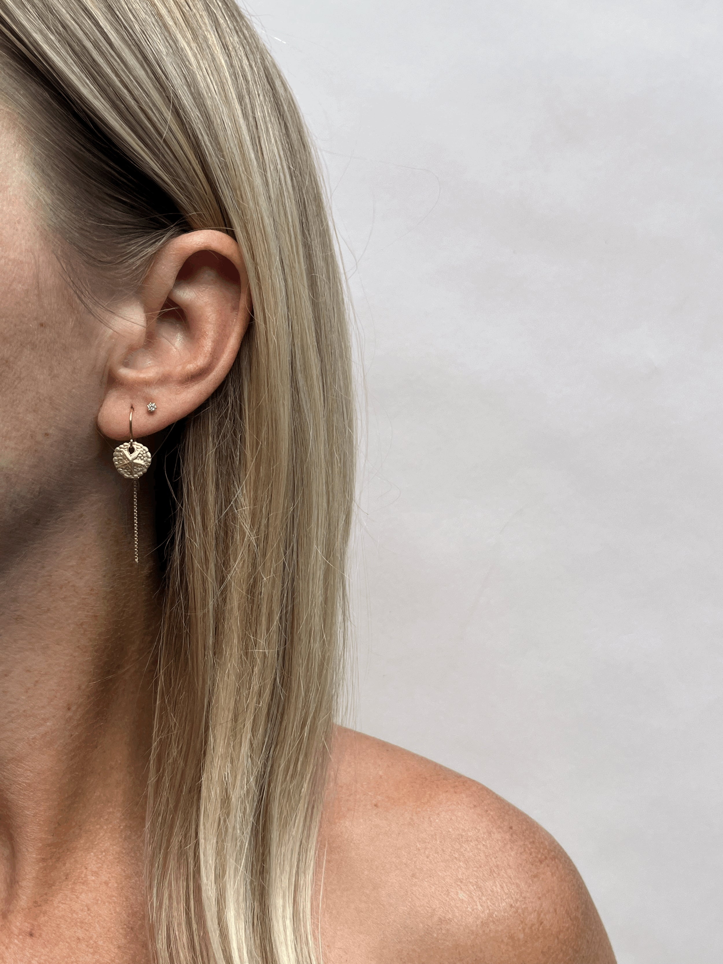 Model wearing a 10mm yellow gold-filled sand dollar threader earring in her first ear piercing and a small clear crystal stud earring in her second piercing