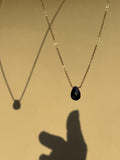 Dark blue natural sapphire stone drop necklace in yellow gold-filled suspended in the air with a shadow of fingers reaching out towards the necklace