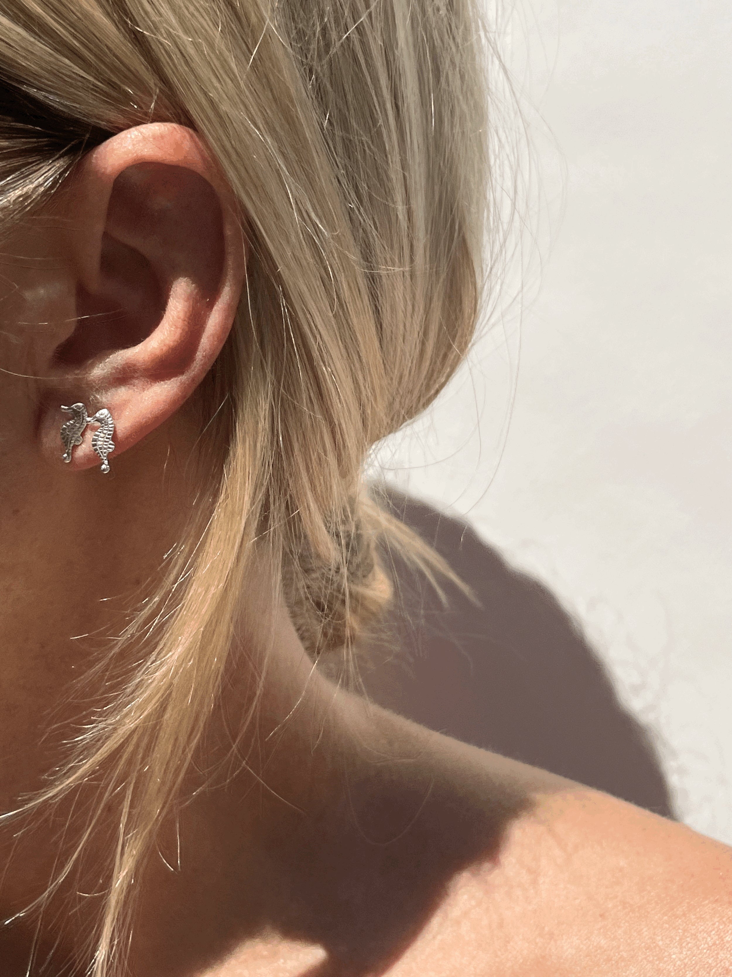 Model wearing sterling silver seahorse studs in both her first and second ear piercings