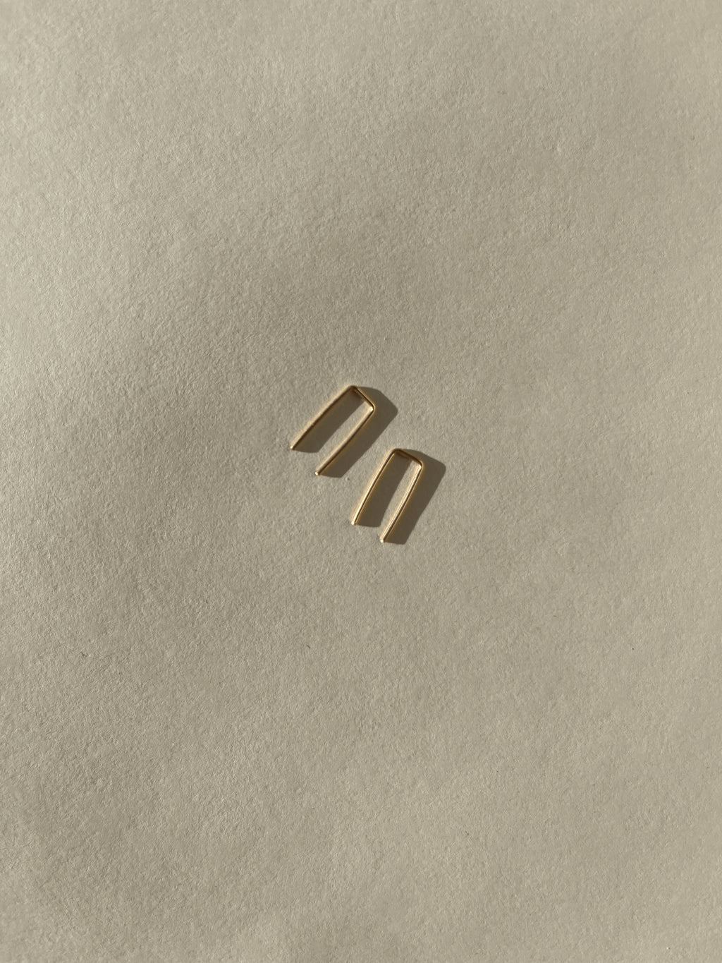 Close-up of yellow gold-filled Staple Earrings on a neutral backdrop, showing their sleek, polished finish