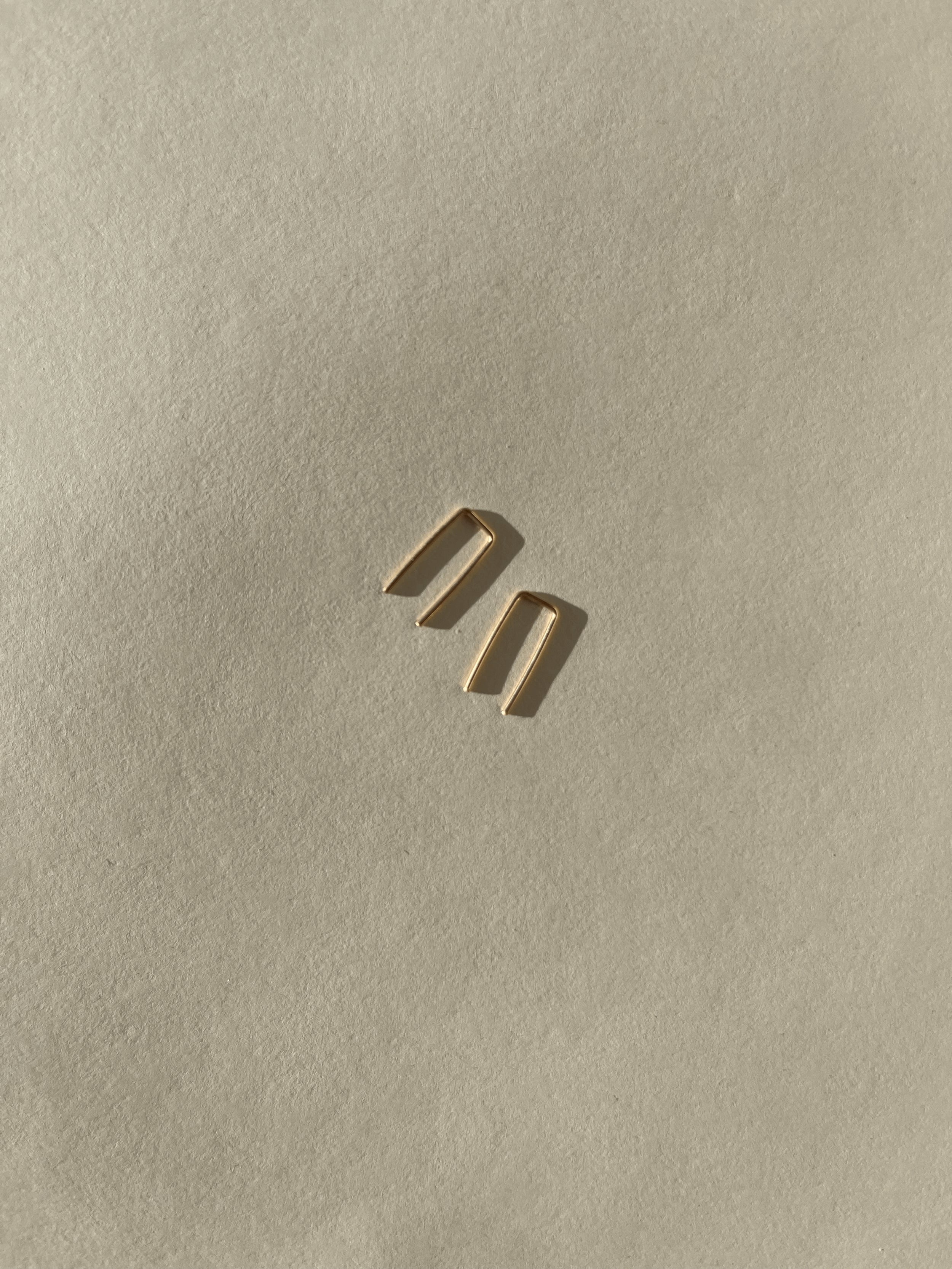 Close-up of yellow gold-filled Staple Earrings on a neutral backdrop, showing their sleek, polished finish