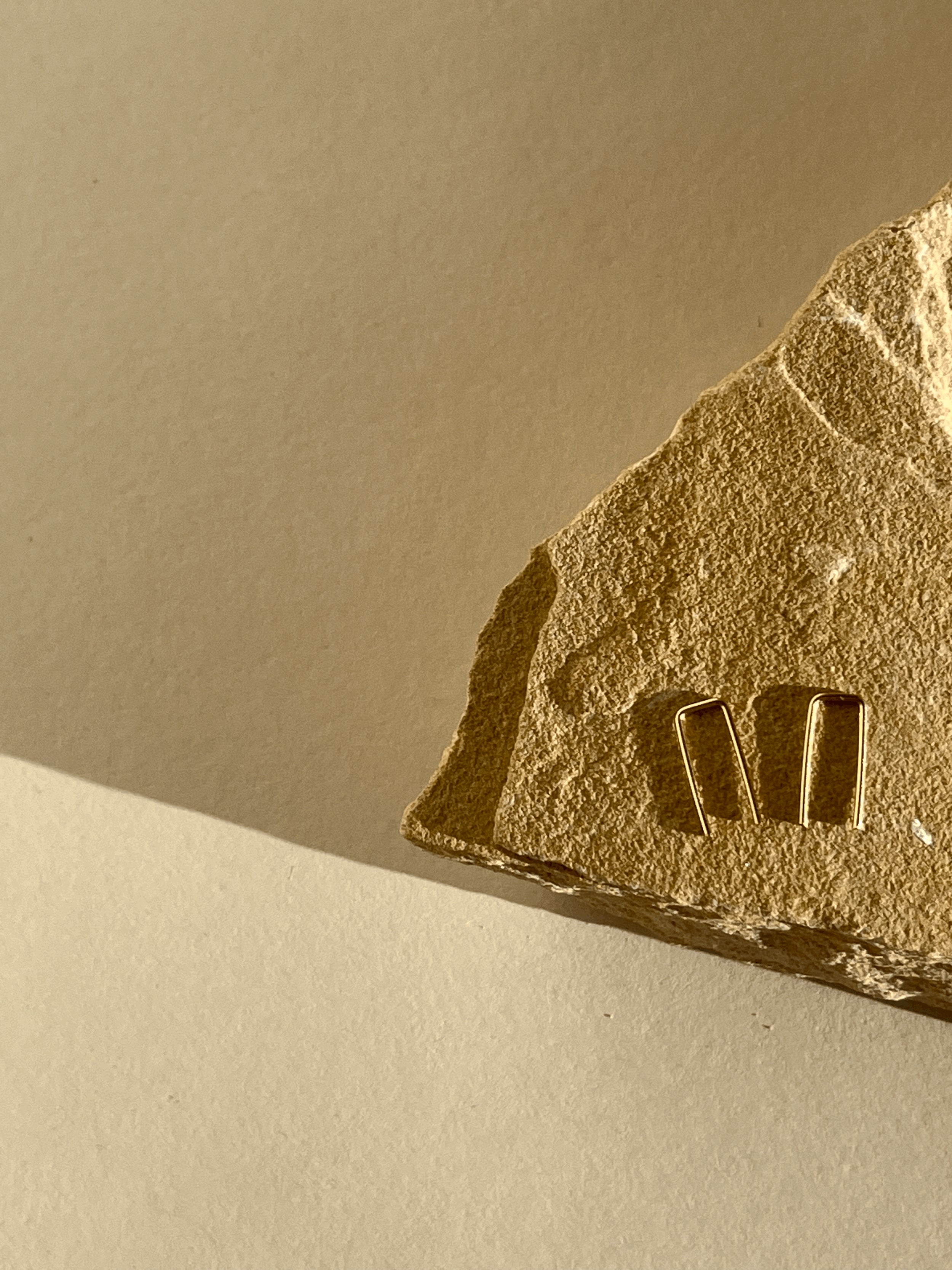 Yellow gold-filled Petite Staple Earrings resting on a natural rock, showcasing their delicate size and texture
