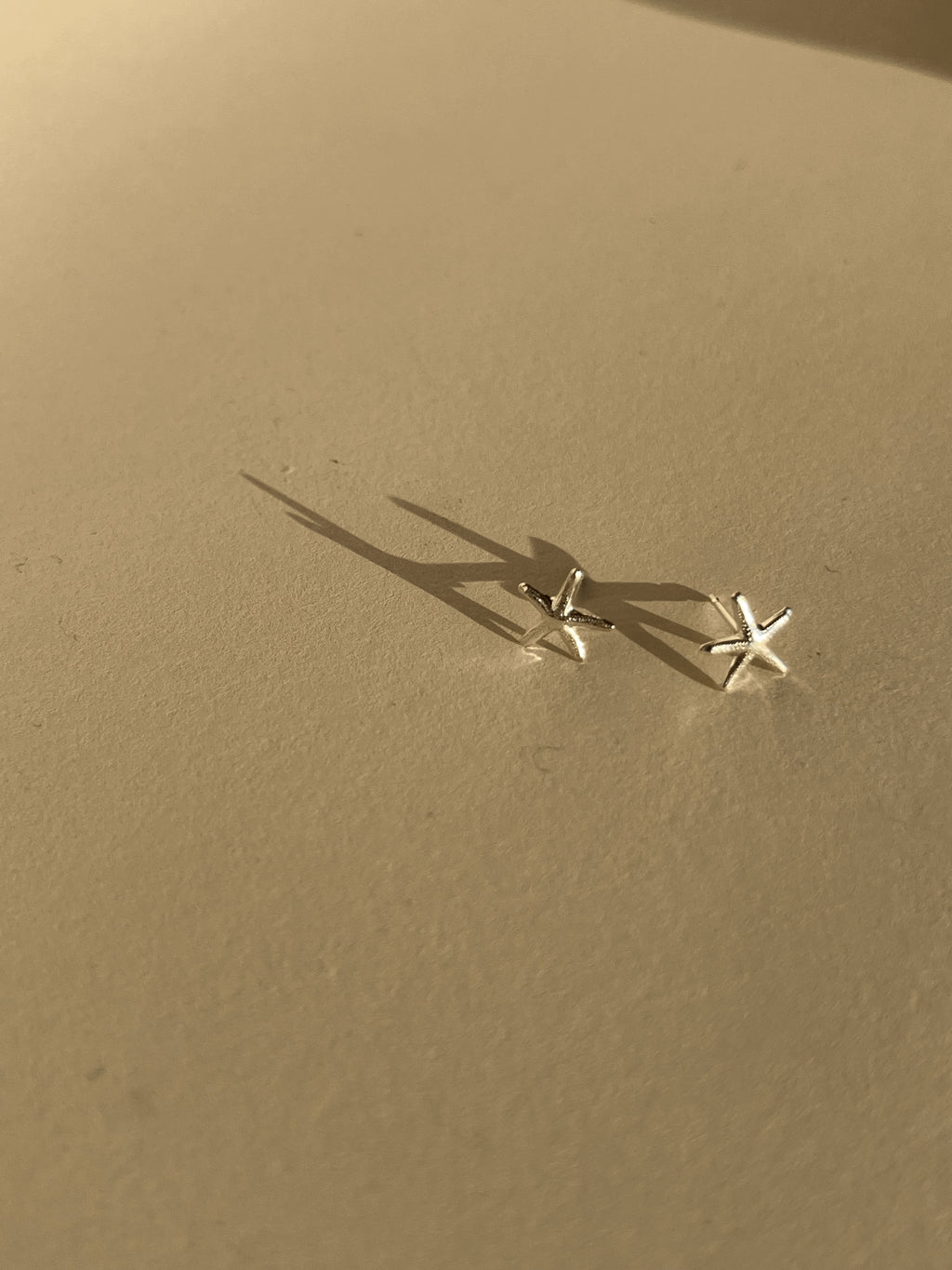 Pair of skinny sterling silver starfish stud earrings on a neutral background