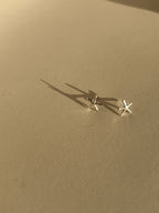 Pair of skinny sterling silver starfish stud earrings on a neutral background