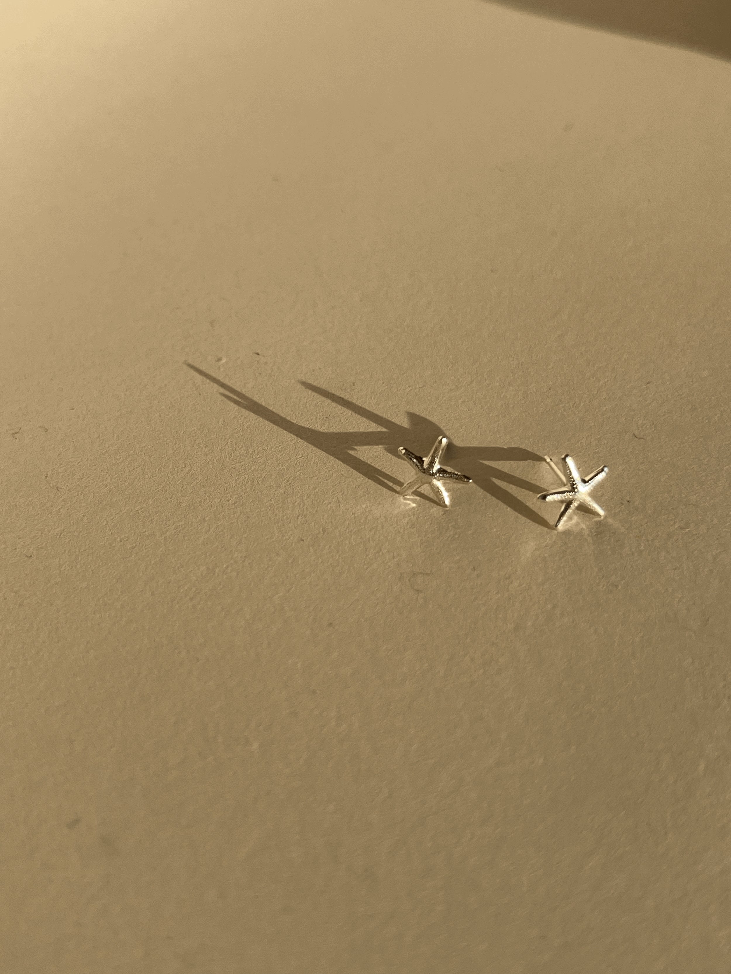 Pair of skinny sterling silver starfish stud earrings on a neutral background