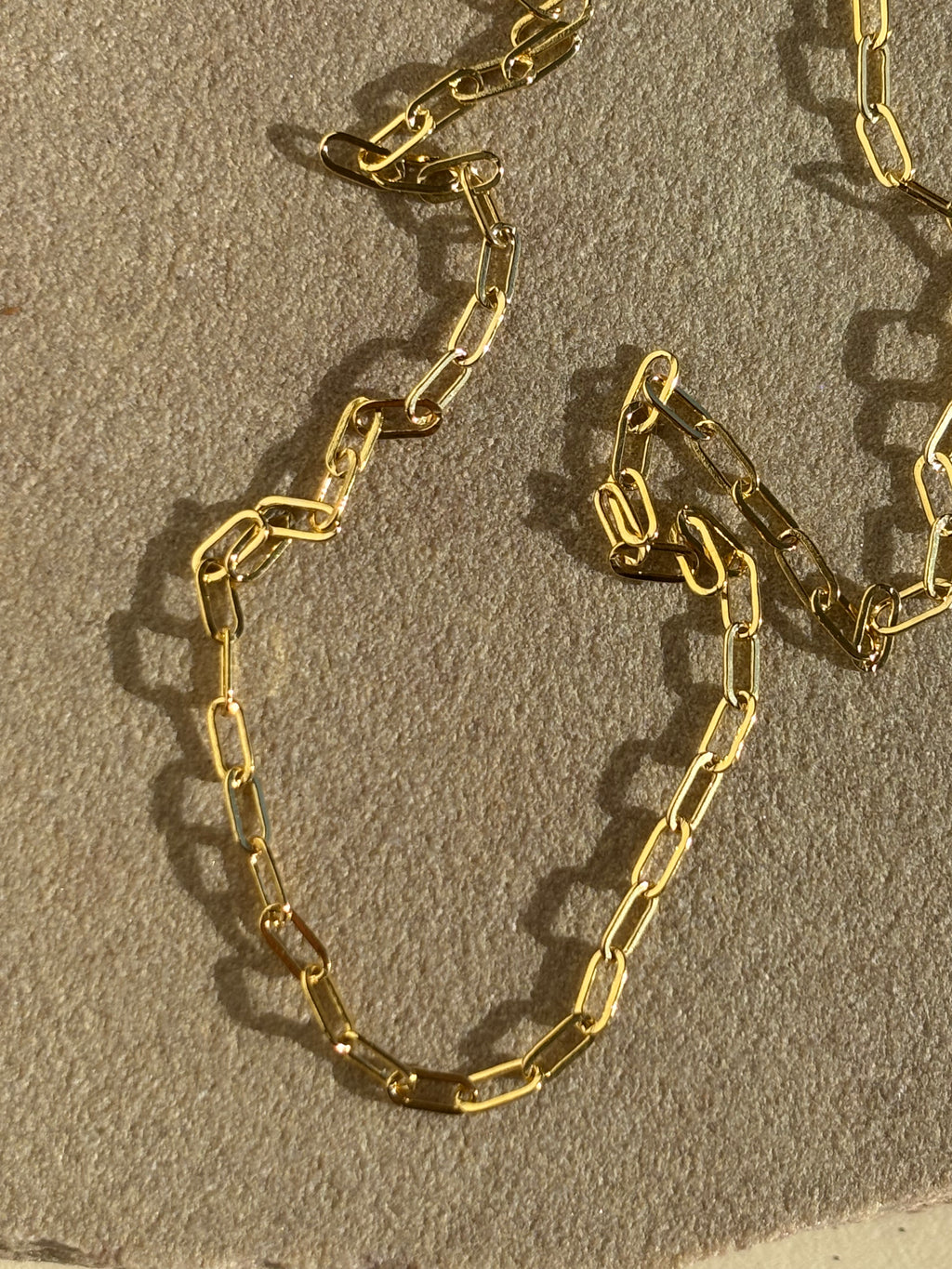 Close-up of Thalken's small link paperclip necklace in yellow gold-filled on a rock in warm light
