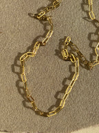 Close-up of Thalken's small link paperclip necklace in yellow gold-filled on a rock in warm light