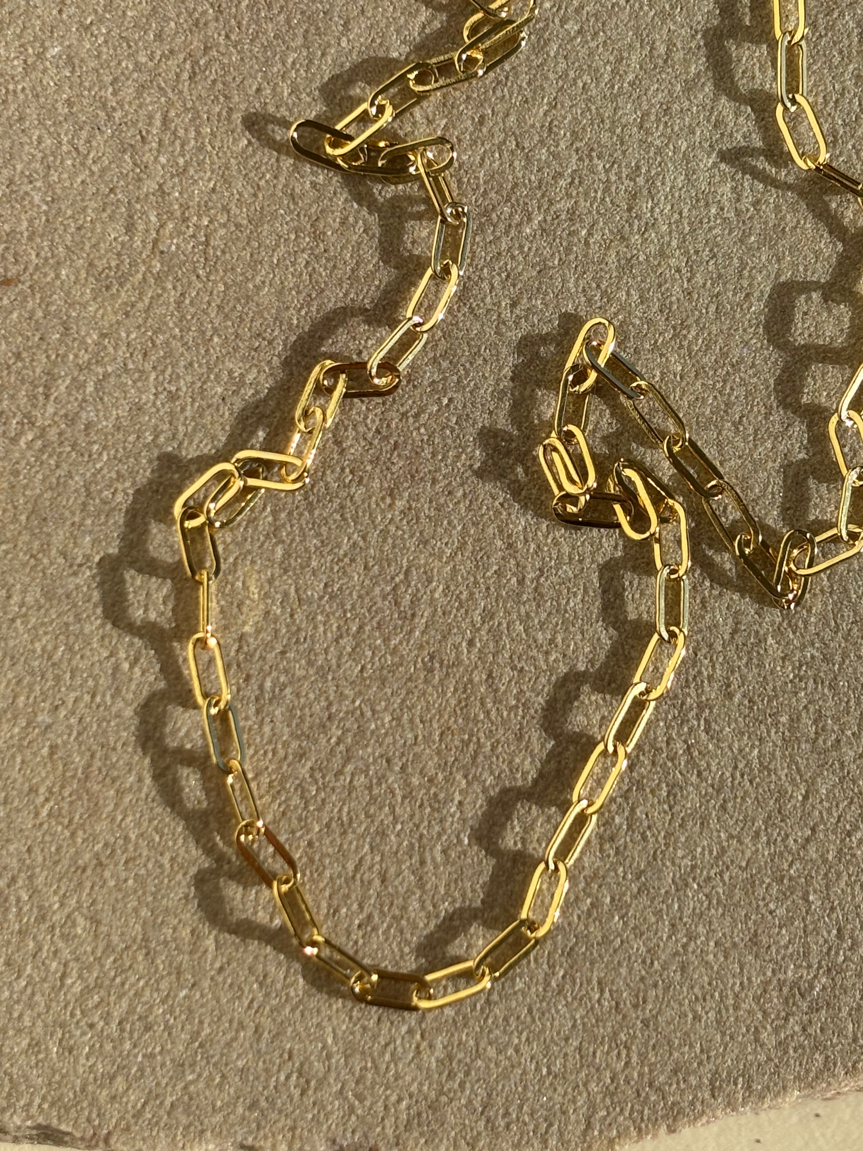 Close-up of Thalken's small link paperclip necklace in yellow gold-filled on a rock in warm light