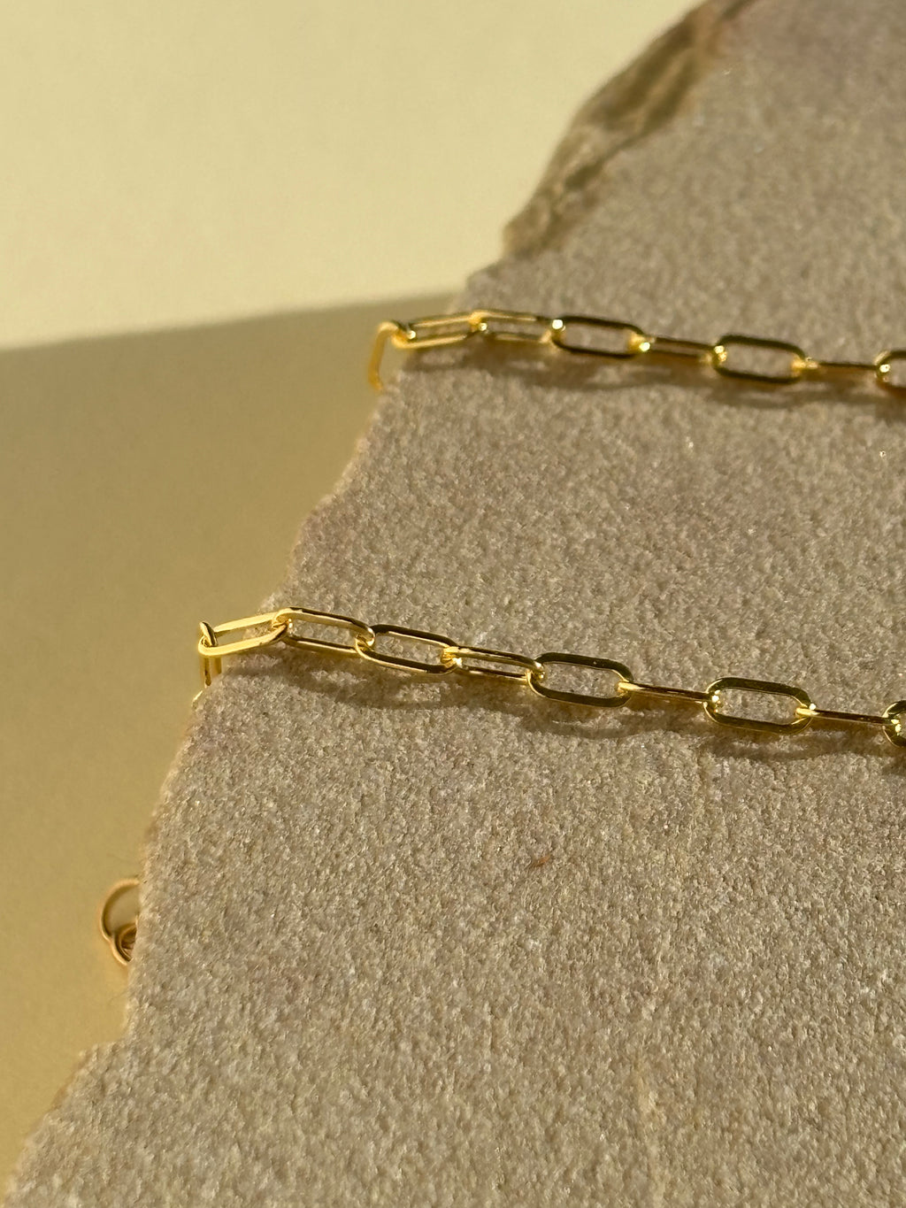 Close-up of Thalken's small link paperclip necklace in yellow gold-filled on a rock in warm light