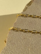 Close-up of Thalken's small link paperclip necklace in yellow gold-filled on a rock in warm light