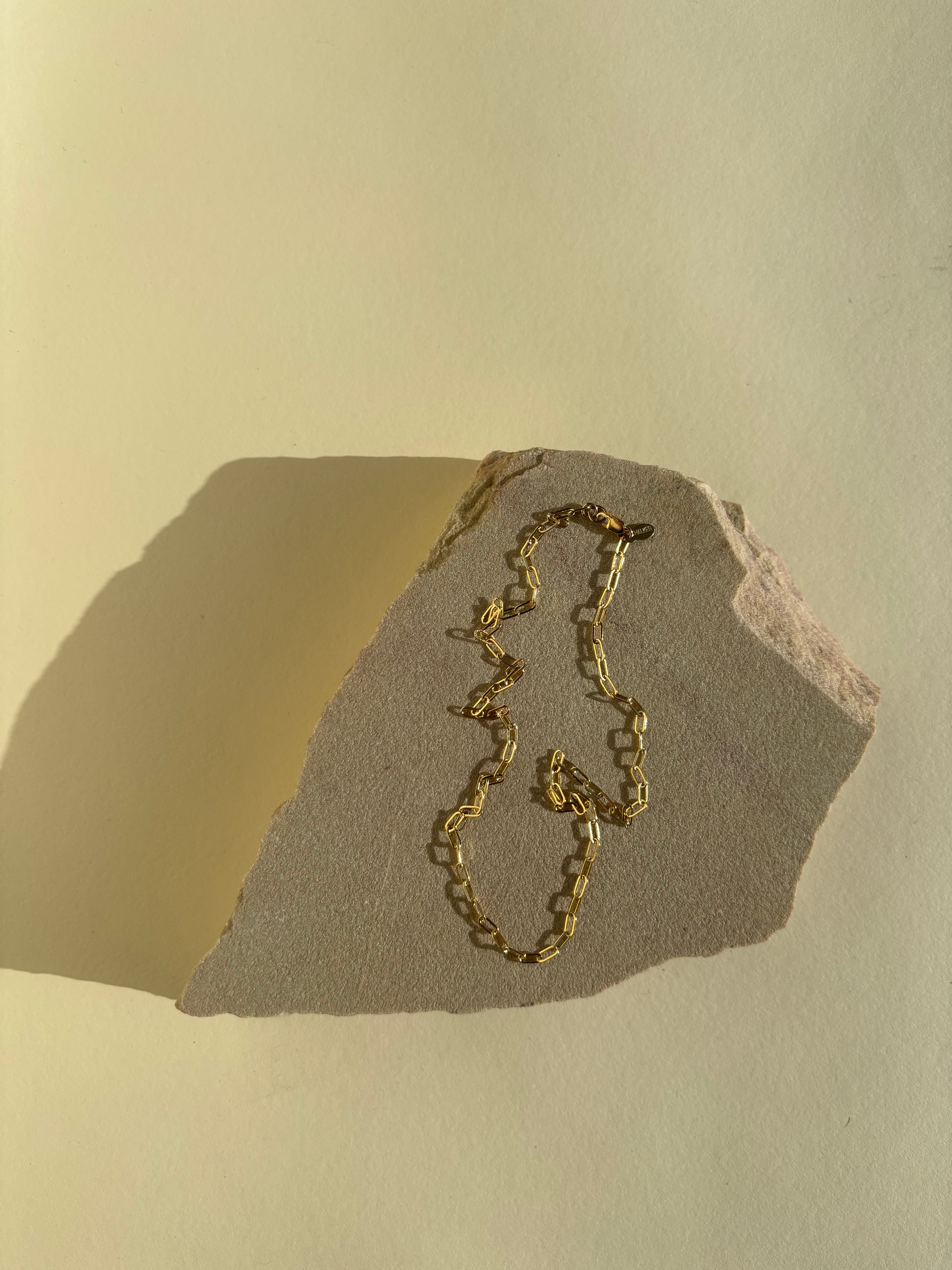 Thalken's small link paperclip necklace in yellow gold-filled on a rock in warm light