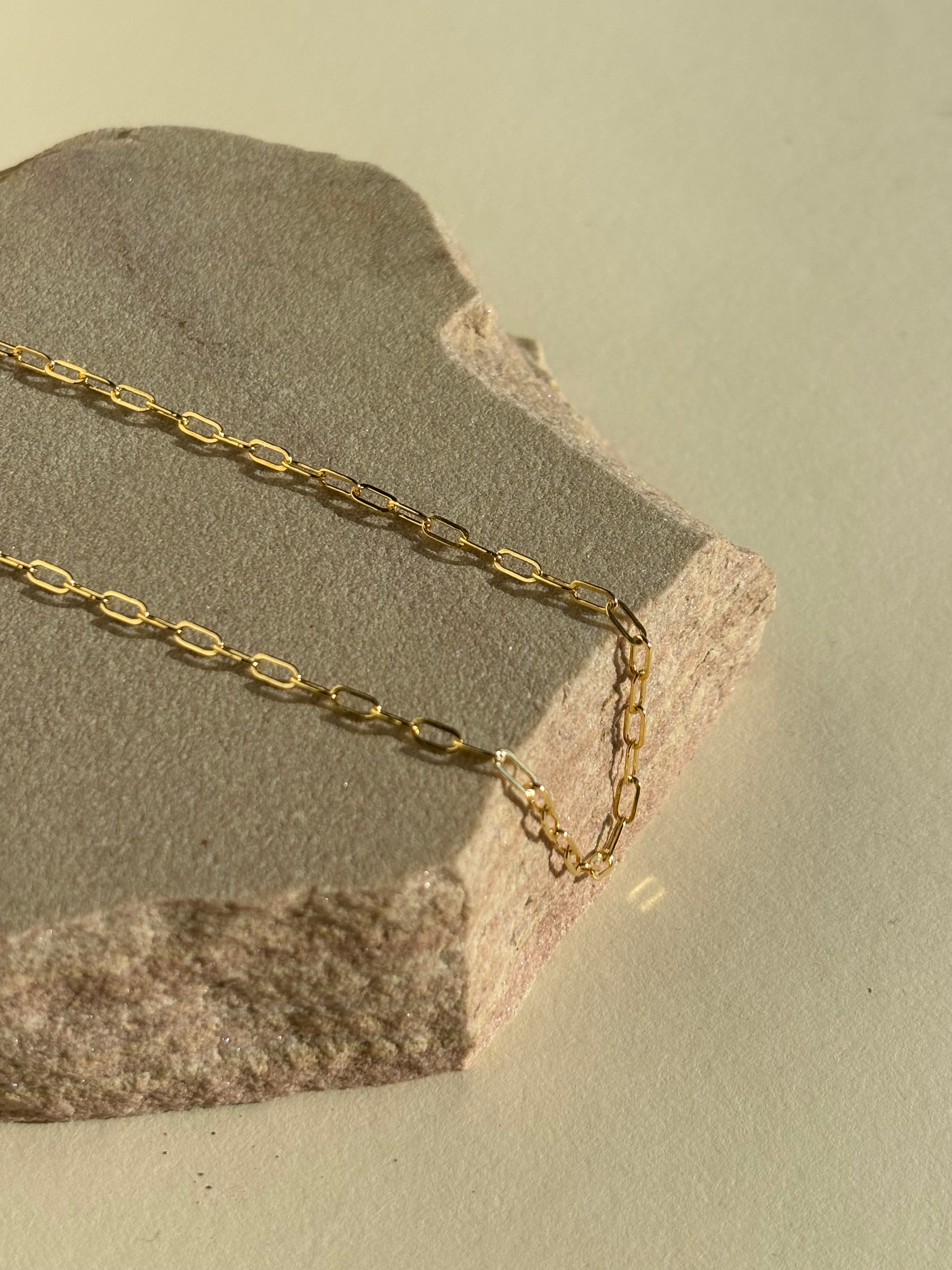 Thalken's small link paperclip necklace in yellow gold-filled on a rock in warm light
