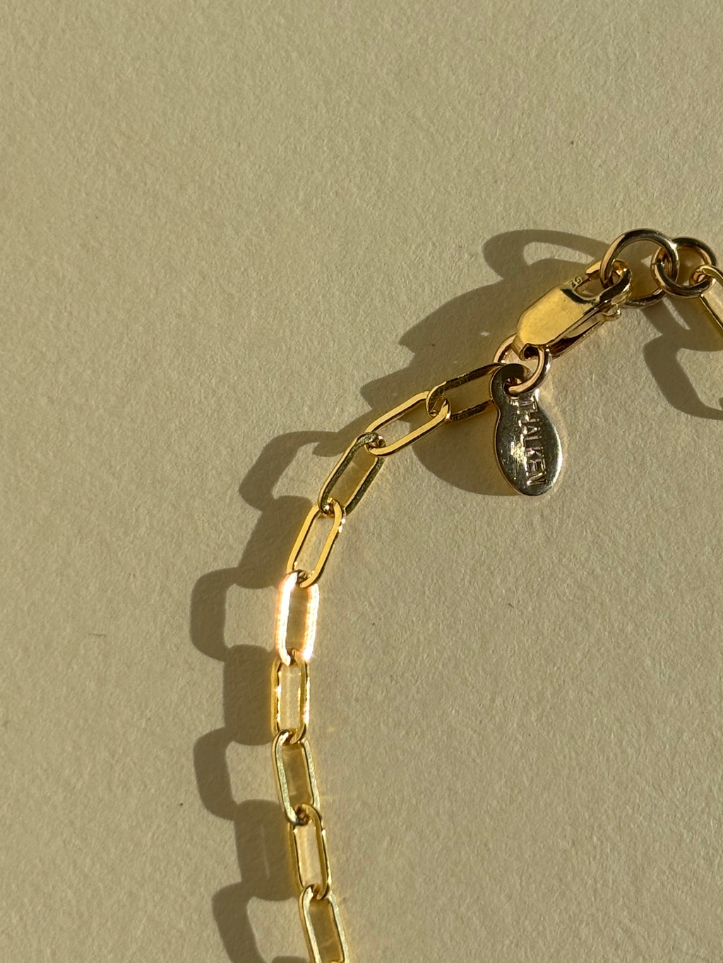 Close-up of metal THALKEN tag detail of Thalken's small link paperclip necklace